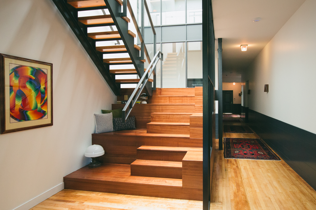 Custom wood staircase and hallway at The Publishing House boutique bed and breakfast with tiered seating, exposed steel, vintage art, and Persian rugs by Siren Betty Design.