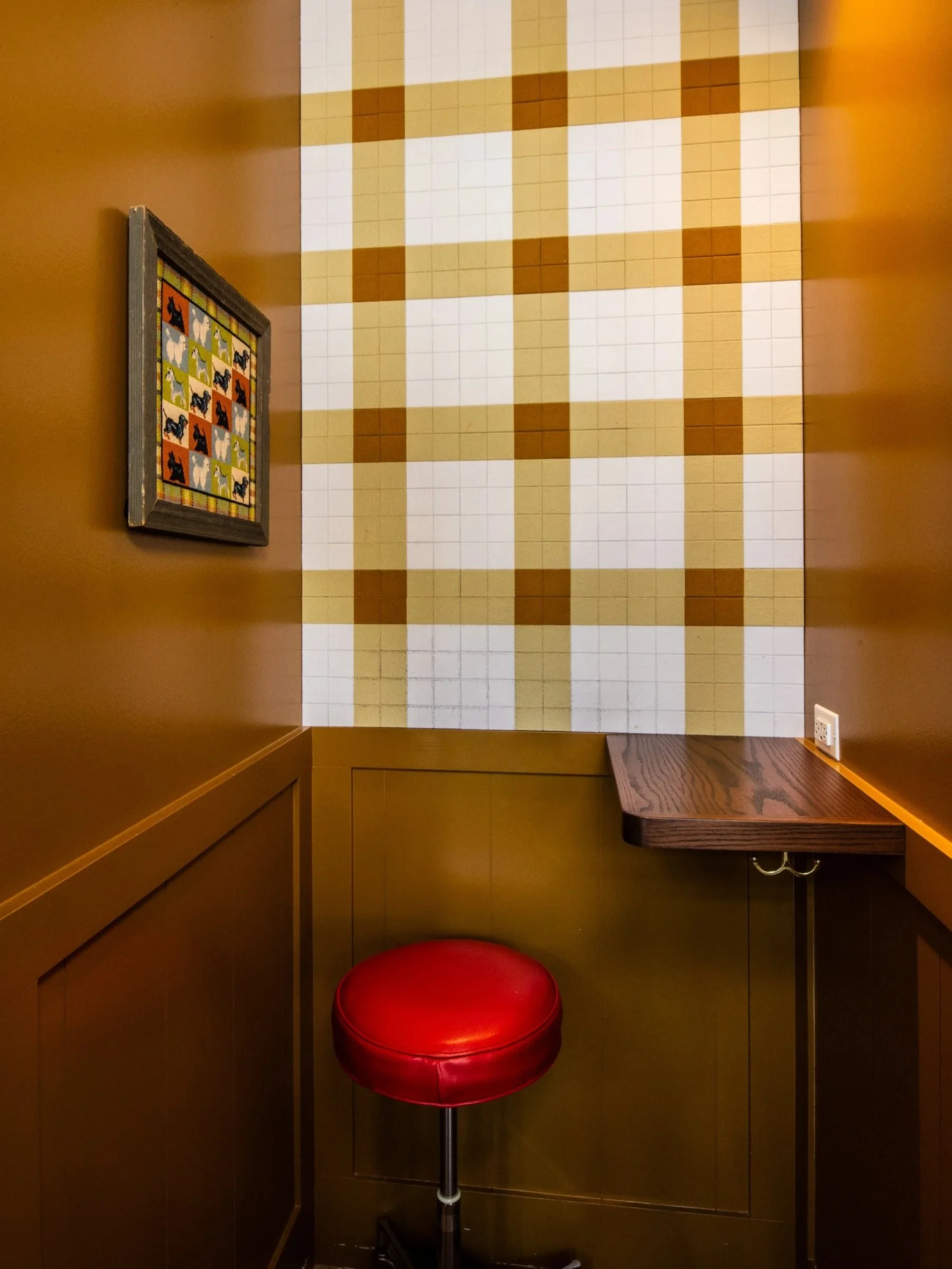 Layla and Ringo’s phone booth with plaid wall, red stool and framed artwork by Siren Betty Design