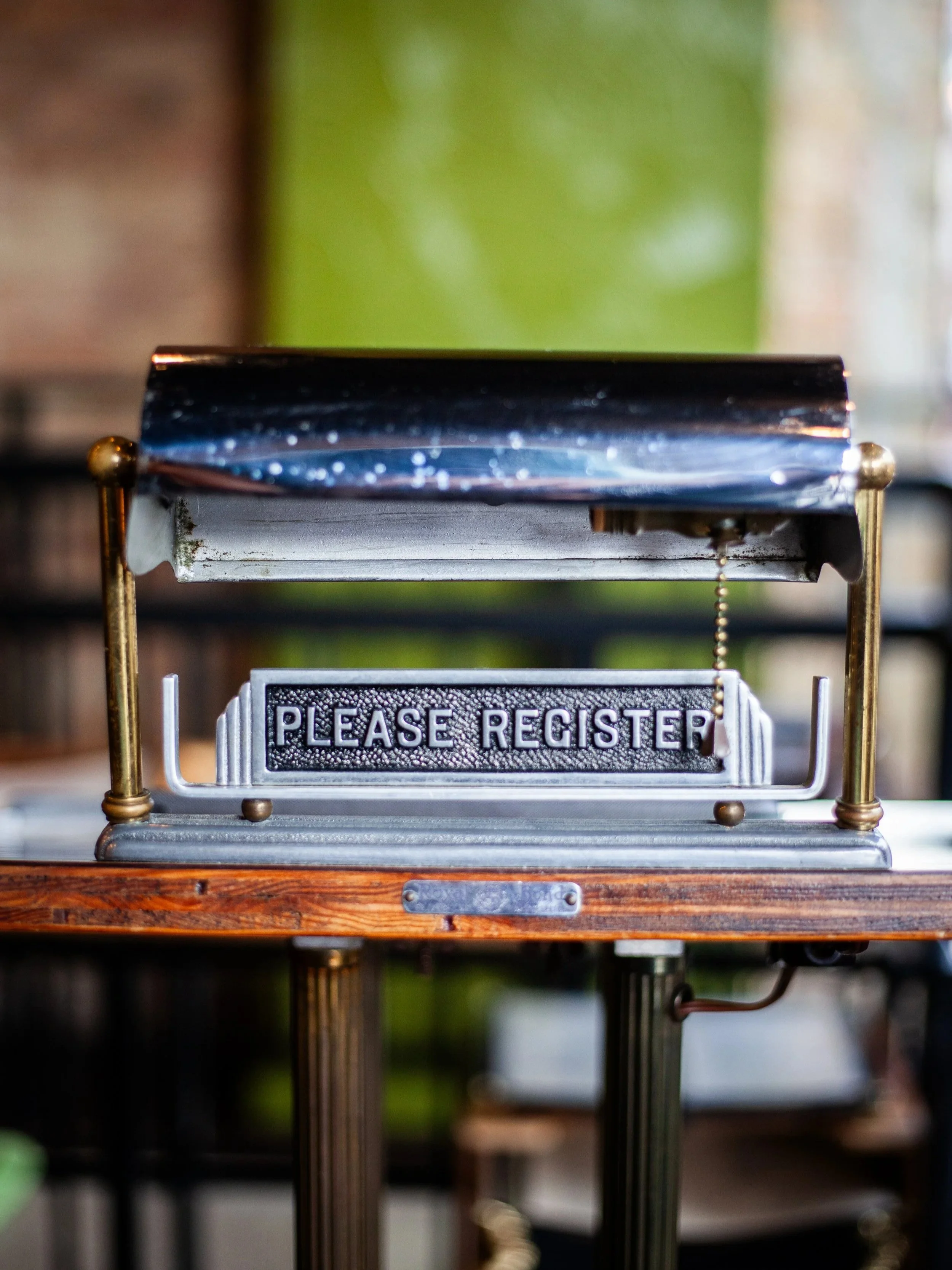 Willow Room vintage “Please Register” sign on a wood counter with brass details styled by Siren Betty Design