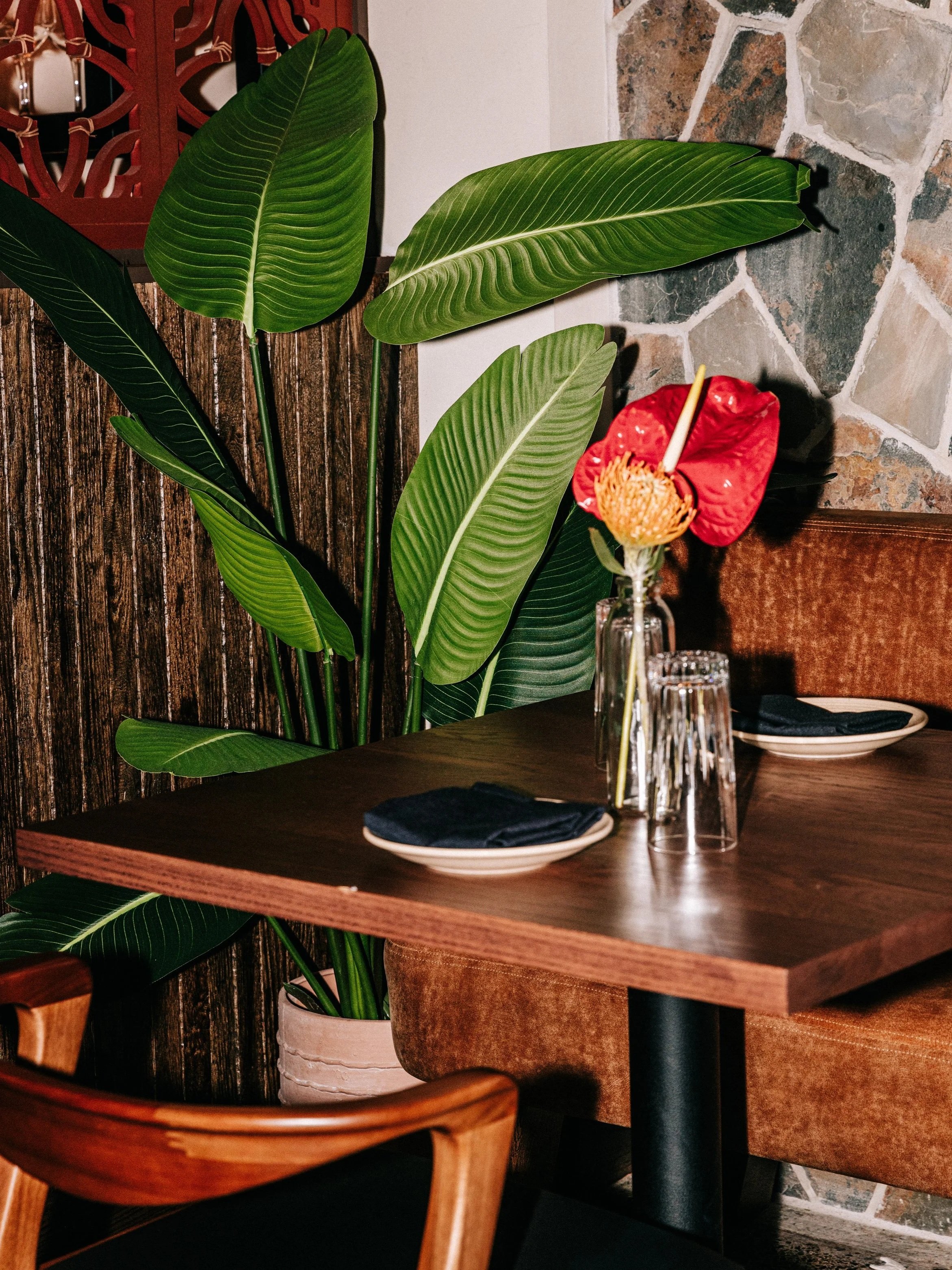 Brasero dining table with tropical plants, floral centerpiece, and warm seating by Siren Betty Design