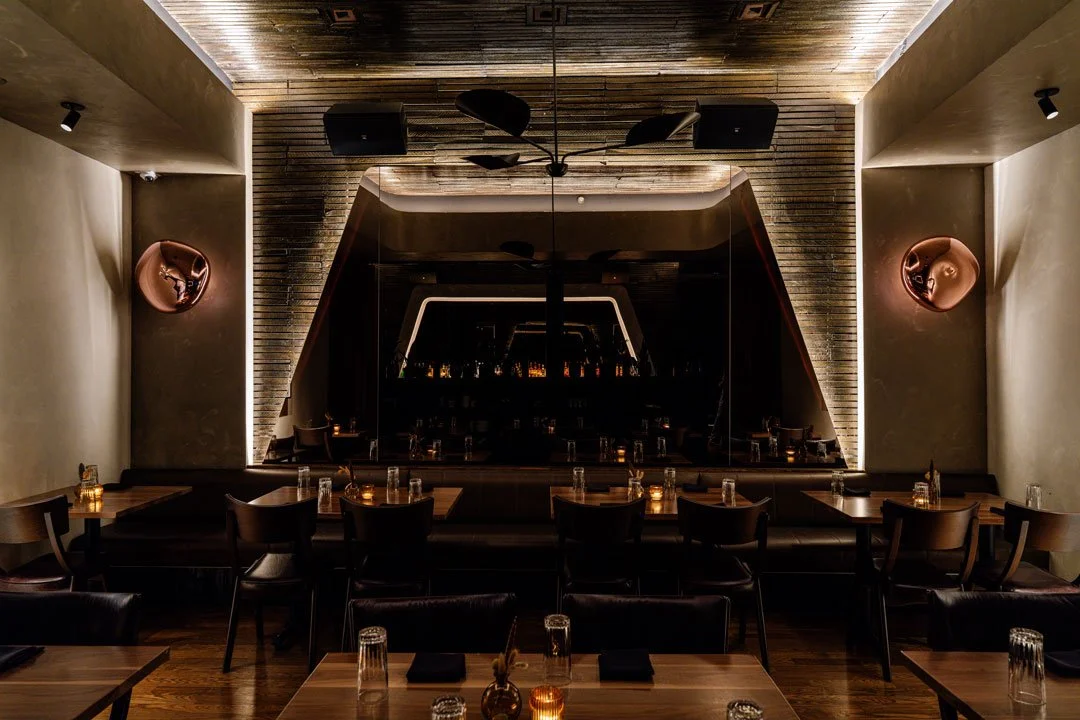 El Che dining room by Siren Betty Design with a dramatic mirrored wall, leather banquettes, warm wood tables, and sculptural lighting.