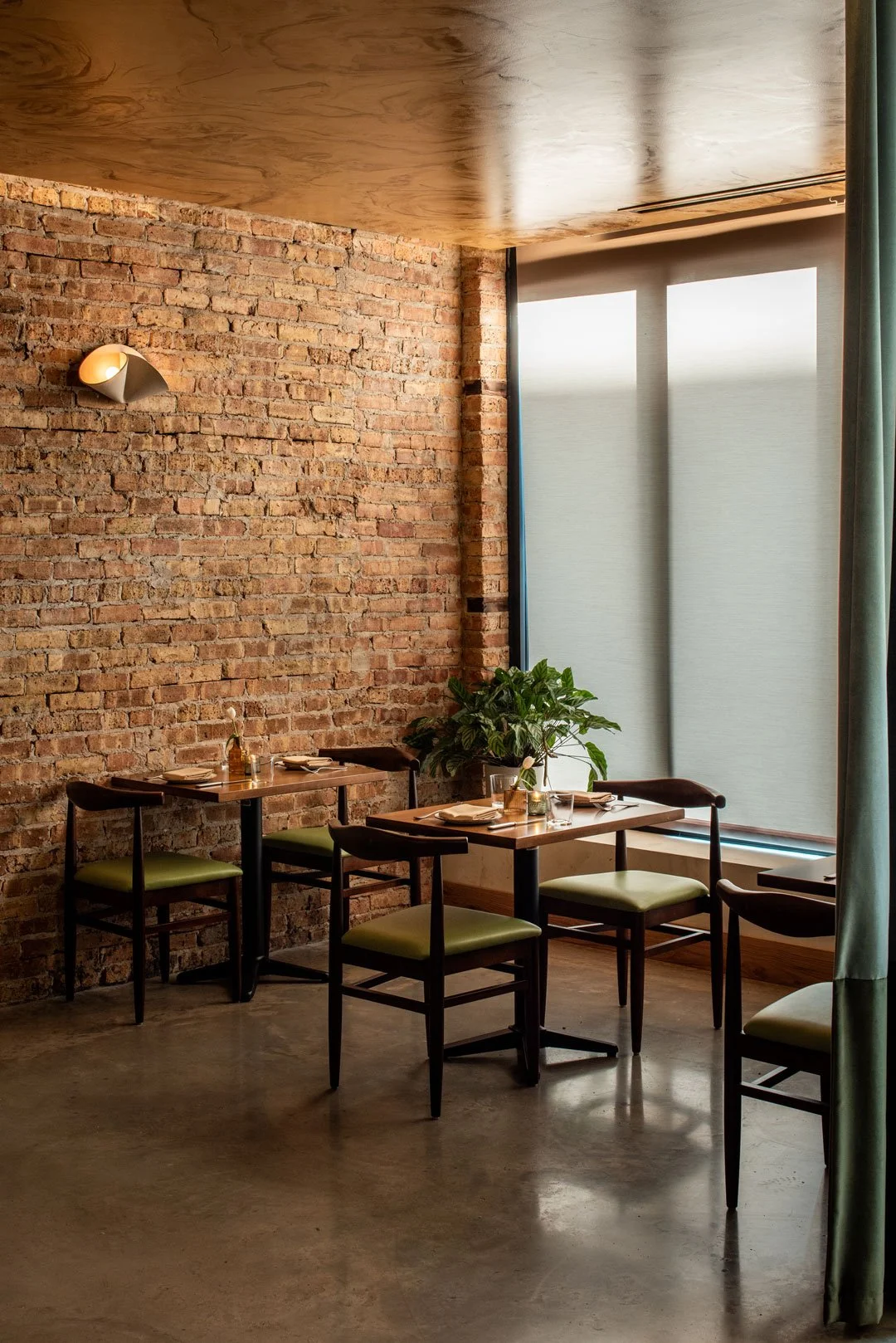 Exposed brick dining room at Burl with dark wood tables, chartreuse seating, and layered restaurant interiors by Siren Betty Design.