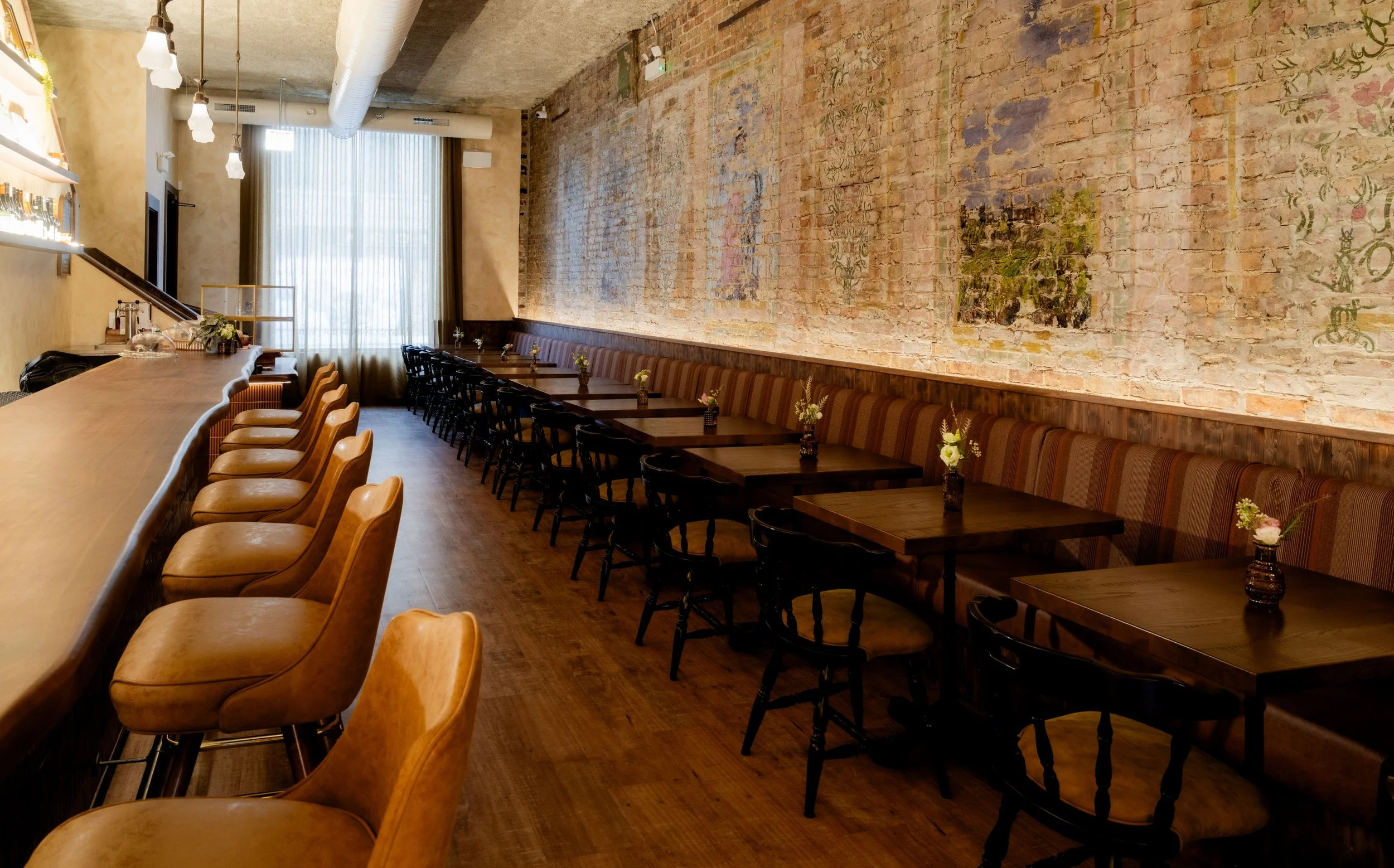 Café Yaya’s bar by Siren Betty Design: long wood counter, leather stools, exposed brick, and vintage mural.
