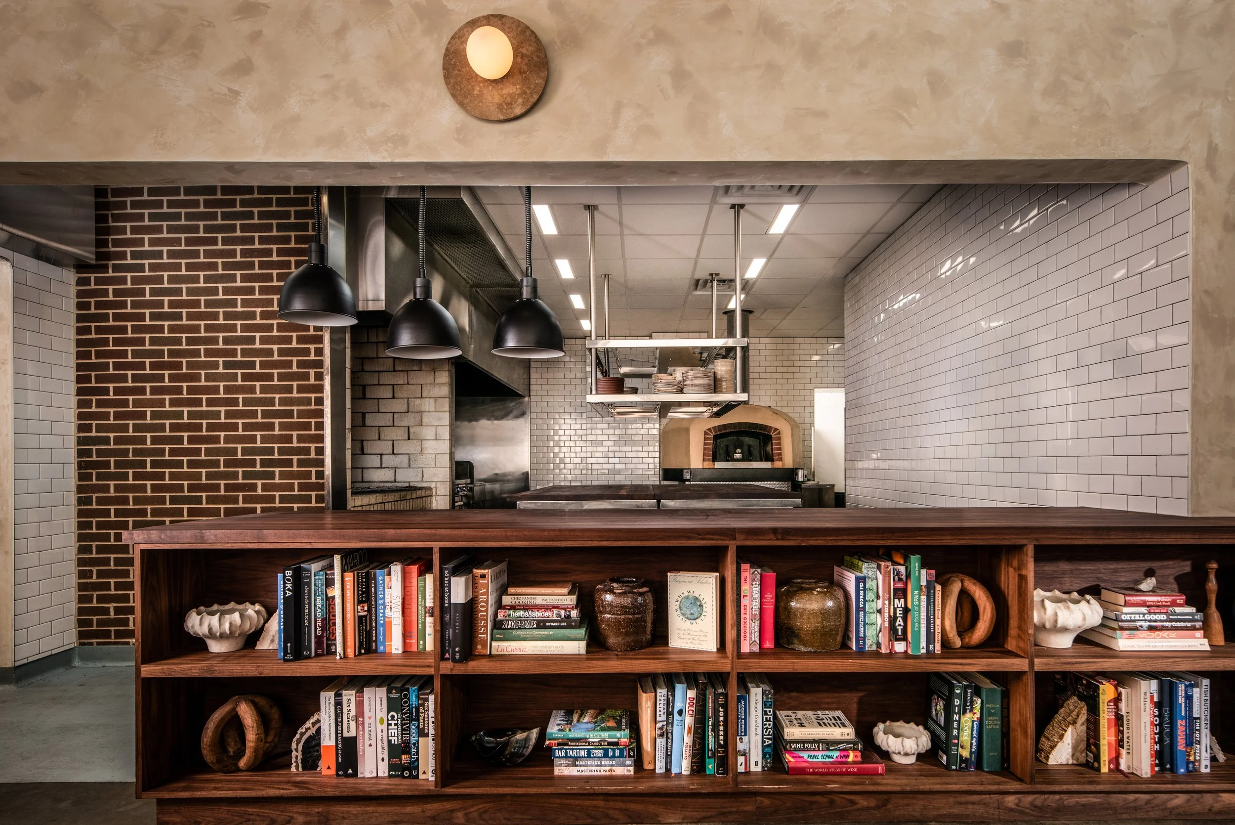 Open wood-fired kitchen at Burl framed by custom walnut shelving, brickwork, and restaurant interior design by Siren Betty Design.