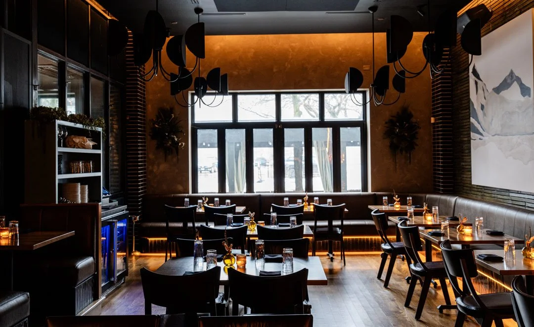 El Che dining room by Siren Betty Design with window banquette seating, sculptural chandeliers, and candlelit tables.
