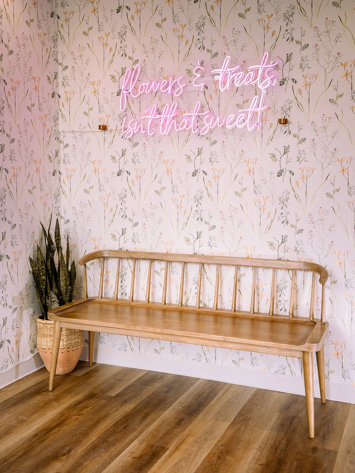Pink neon “flowers & treats” above a blond wood bench and potted snake plant at Après Pastry & Bakery by Siren Betty Design.