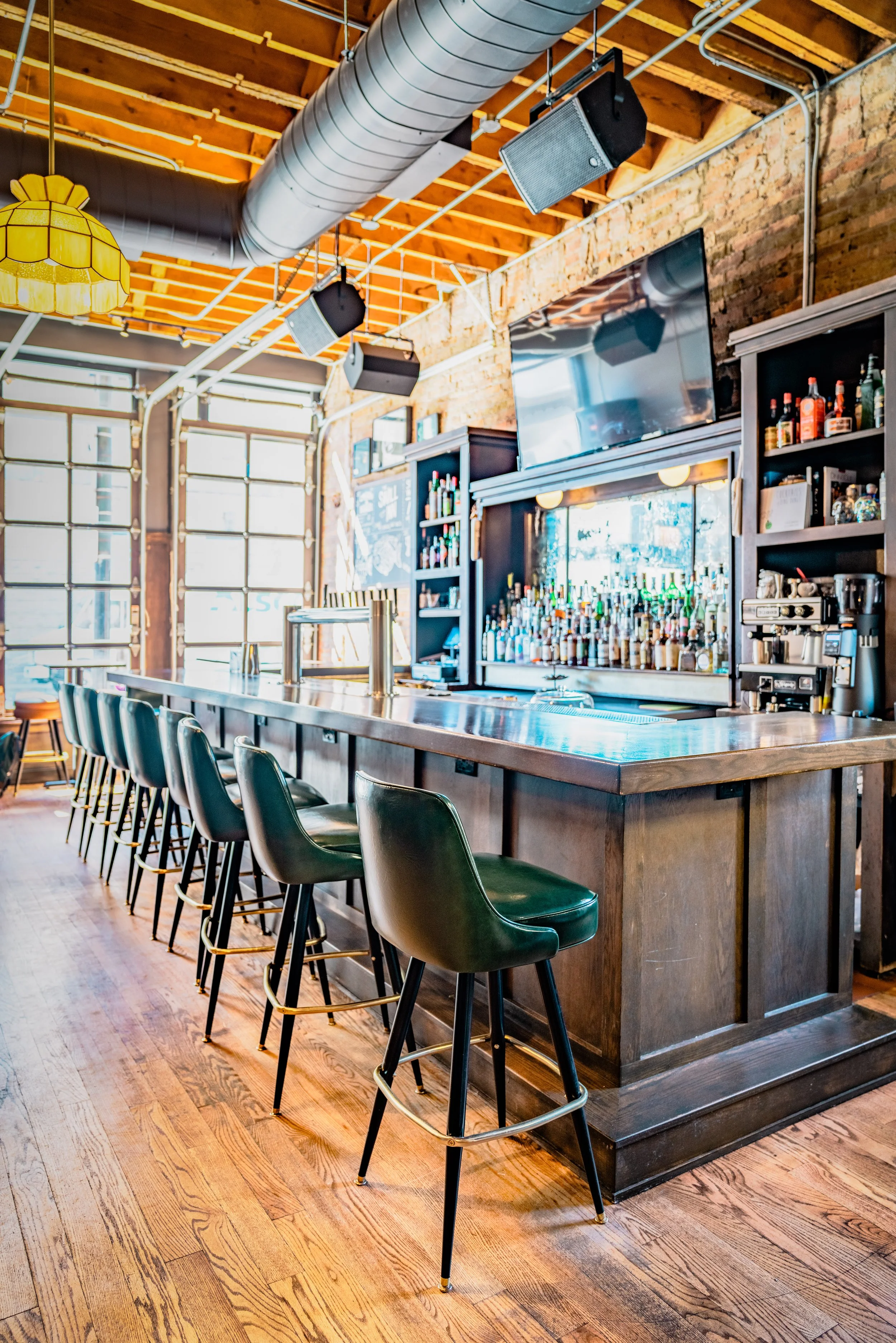 The Swill Inn in Chicago by Siren Betty Design, oak bar with green stools, industrial beams, and vintage charm.