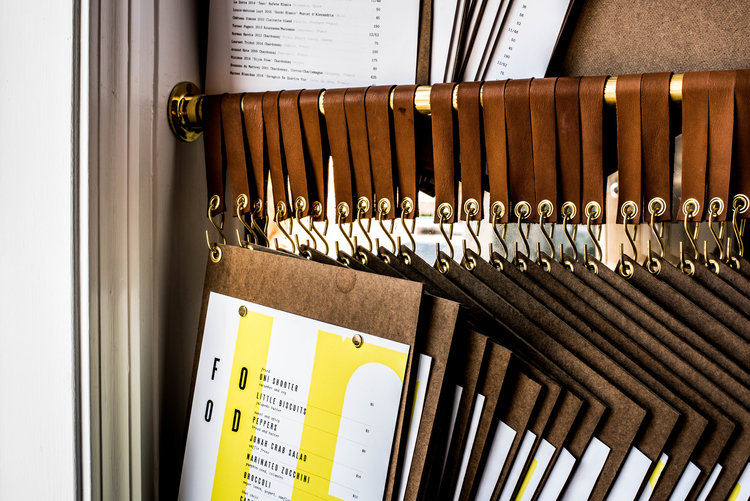 Giant by Siren Betty Design with leather-bound menus featuring yellow accents and brass hardware display.