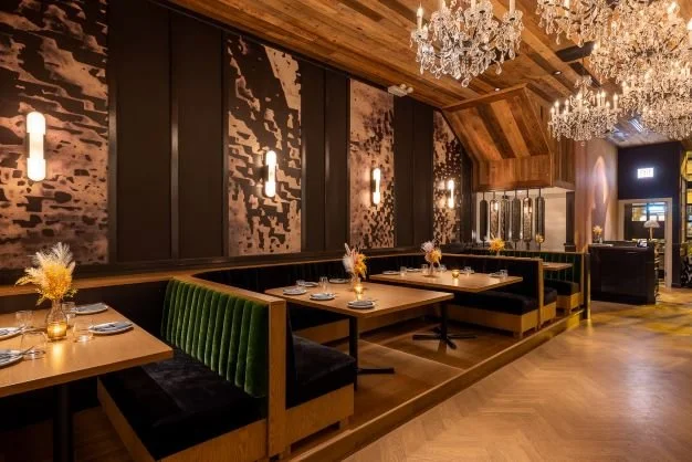 Hide & Seek dining room by Siren Betty Design featuring emerald velvet banquettes, wood ceiling, and sparkling crystal chandeliers.