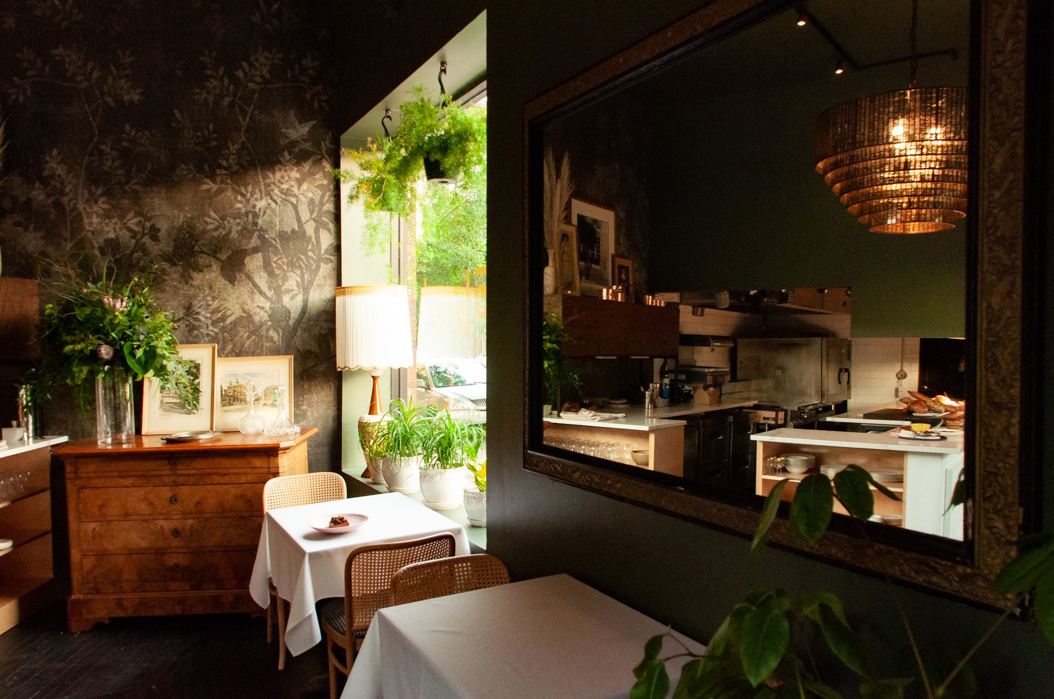 Moody reflection of kitchen and dining space in mirror with floral wallpaper at Robert et Fils by Siren Betty Design.