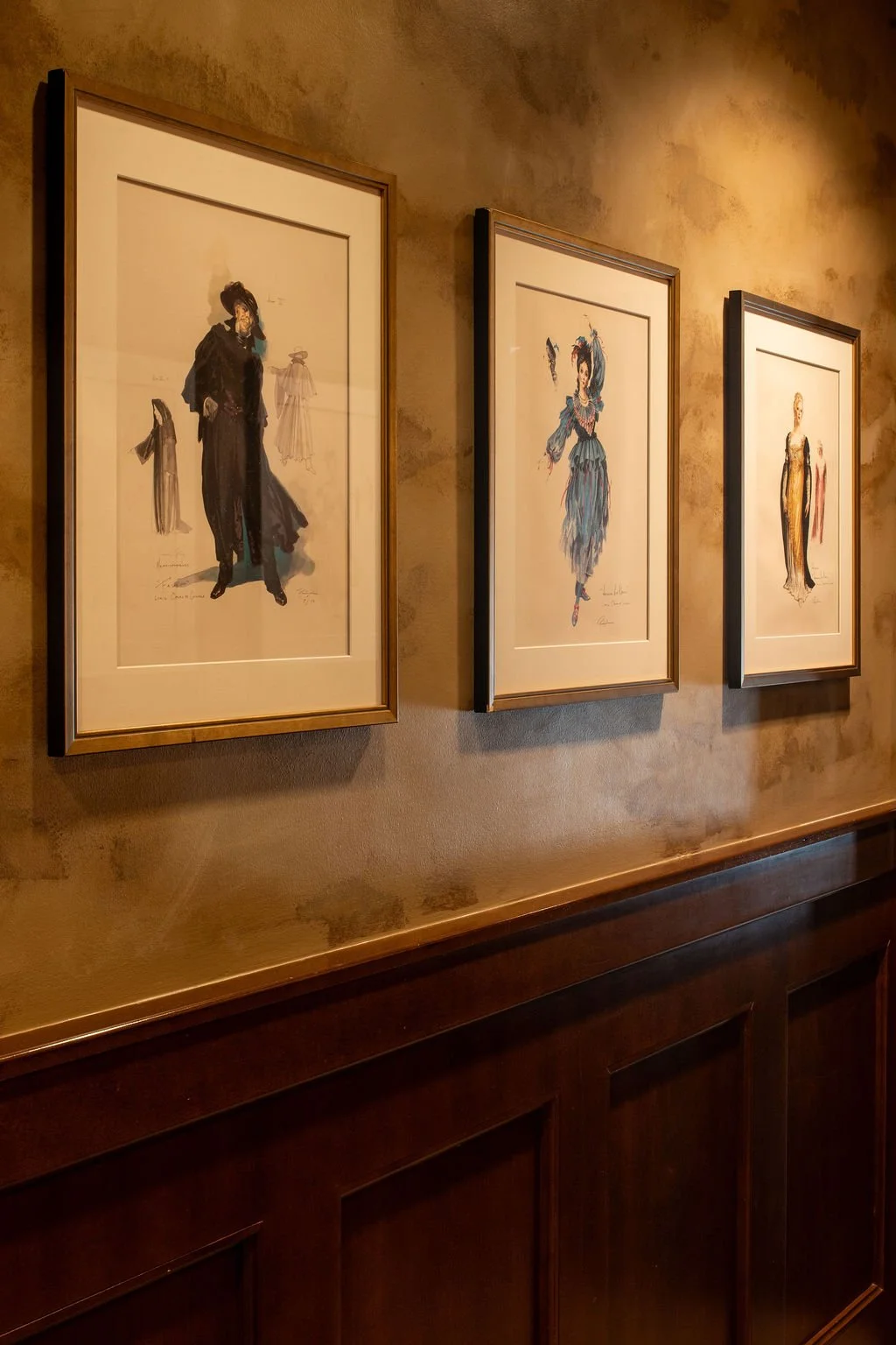 Theatrical costume art and dark wood wainscoting in the Eaves restaurant entry by Siren Betty Design.