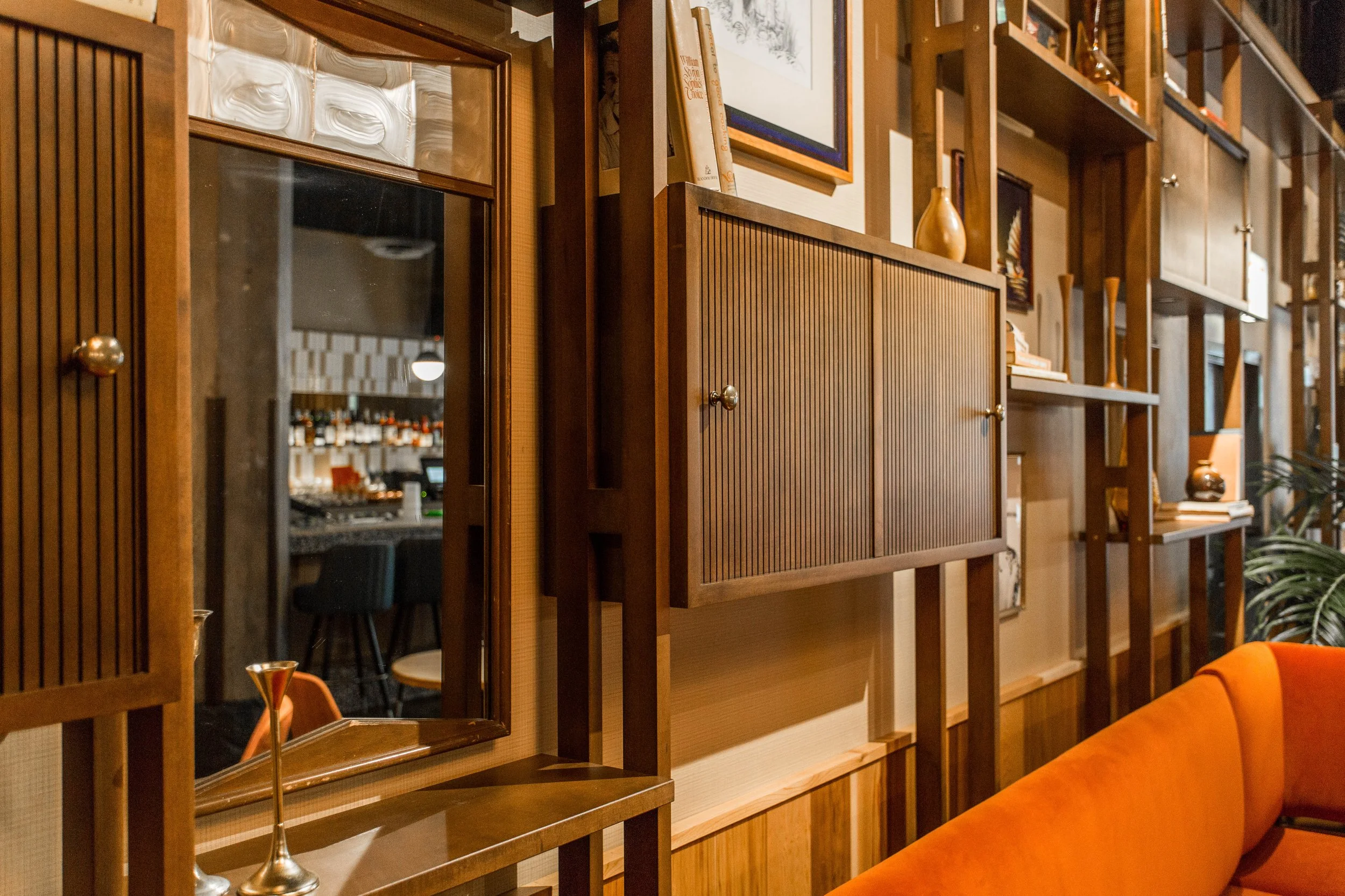 Monty’s Tap by Siren Betty Design, wood shelving with glass panels reflecting bar interior and orange velvet booth.