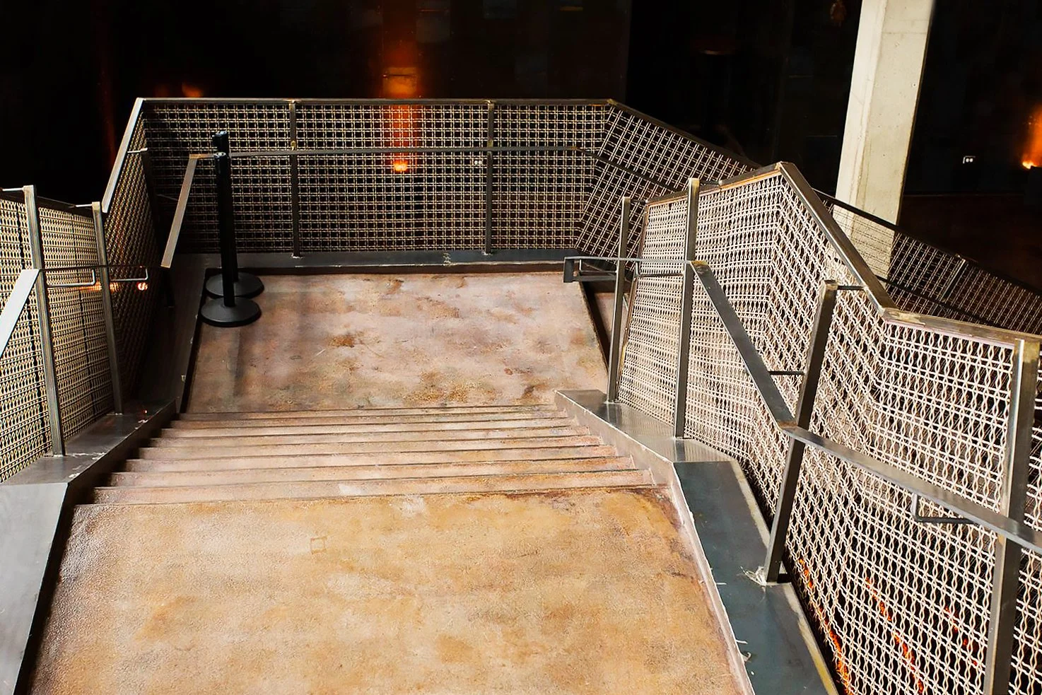 Morgan MFG by Siren Betty Design. Wide stair landing framed by woven-mesh guardrails in a raw-concrete event space.