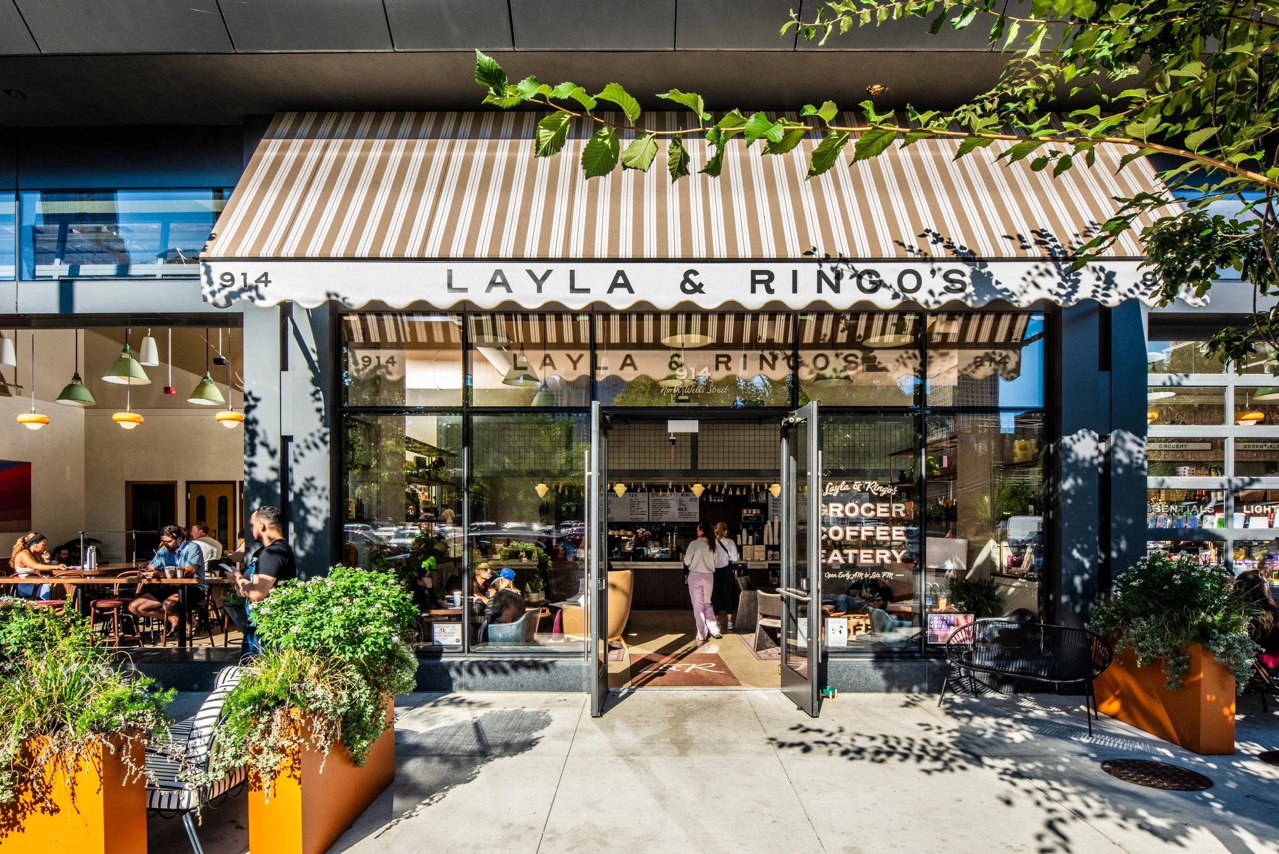 Layla and Ringo’s exterior with striped awning, open café entry, greenery, and street activity by Siren Betty Design