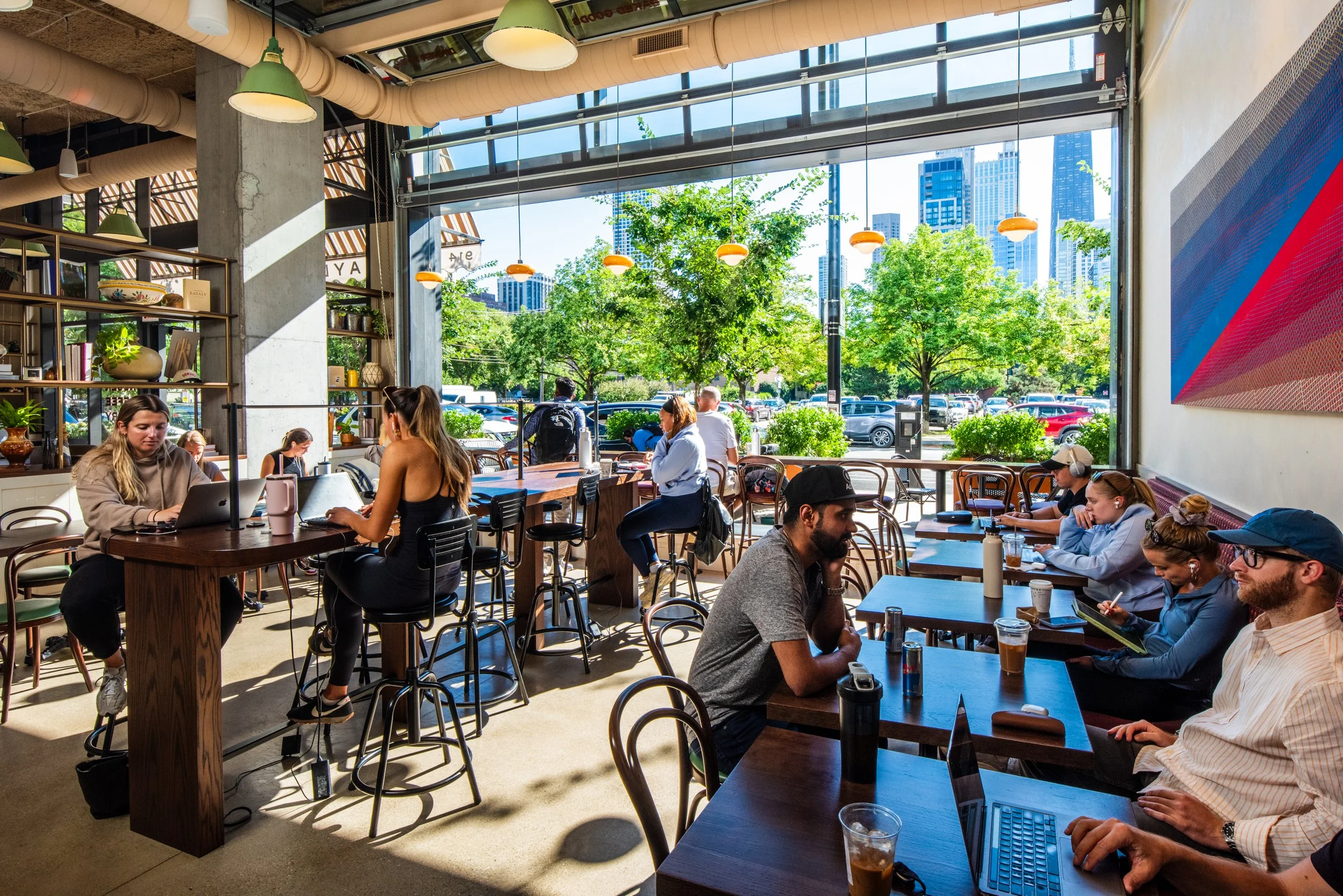 Layla and Ringo’s café seating with guests working, open windows to city views, and warm natural light by Siren Betty Design