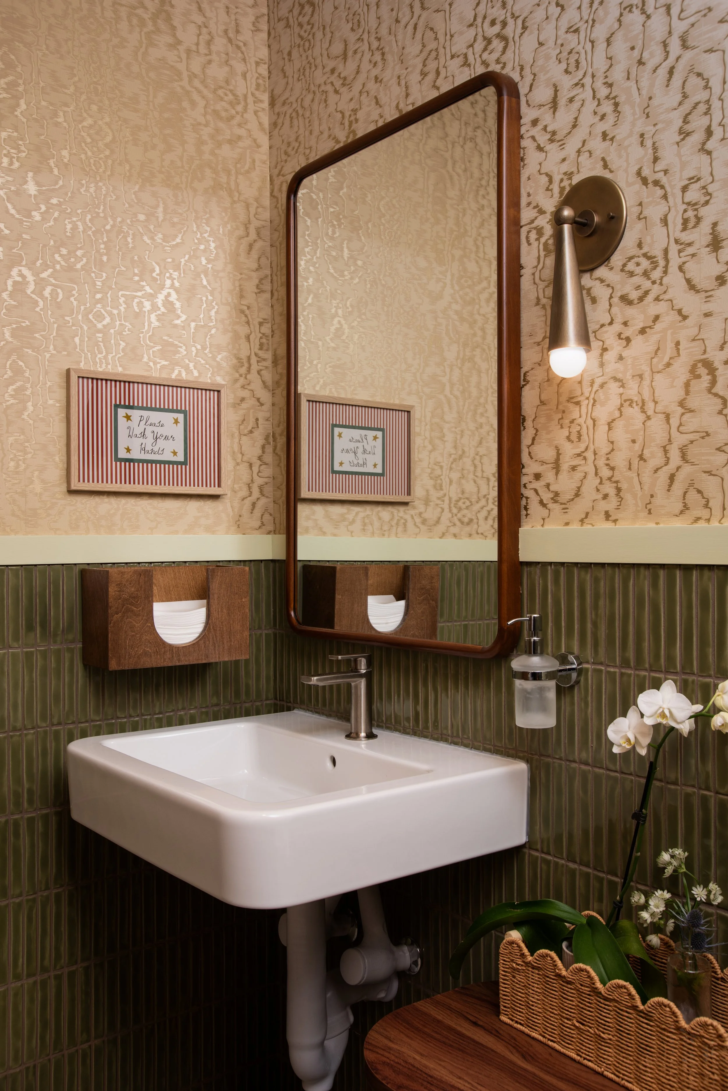Burl restaurant restroom with olive tile, patterned wall covering, a walnut mirror, and decorative lighting by Siren Betty Design.