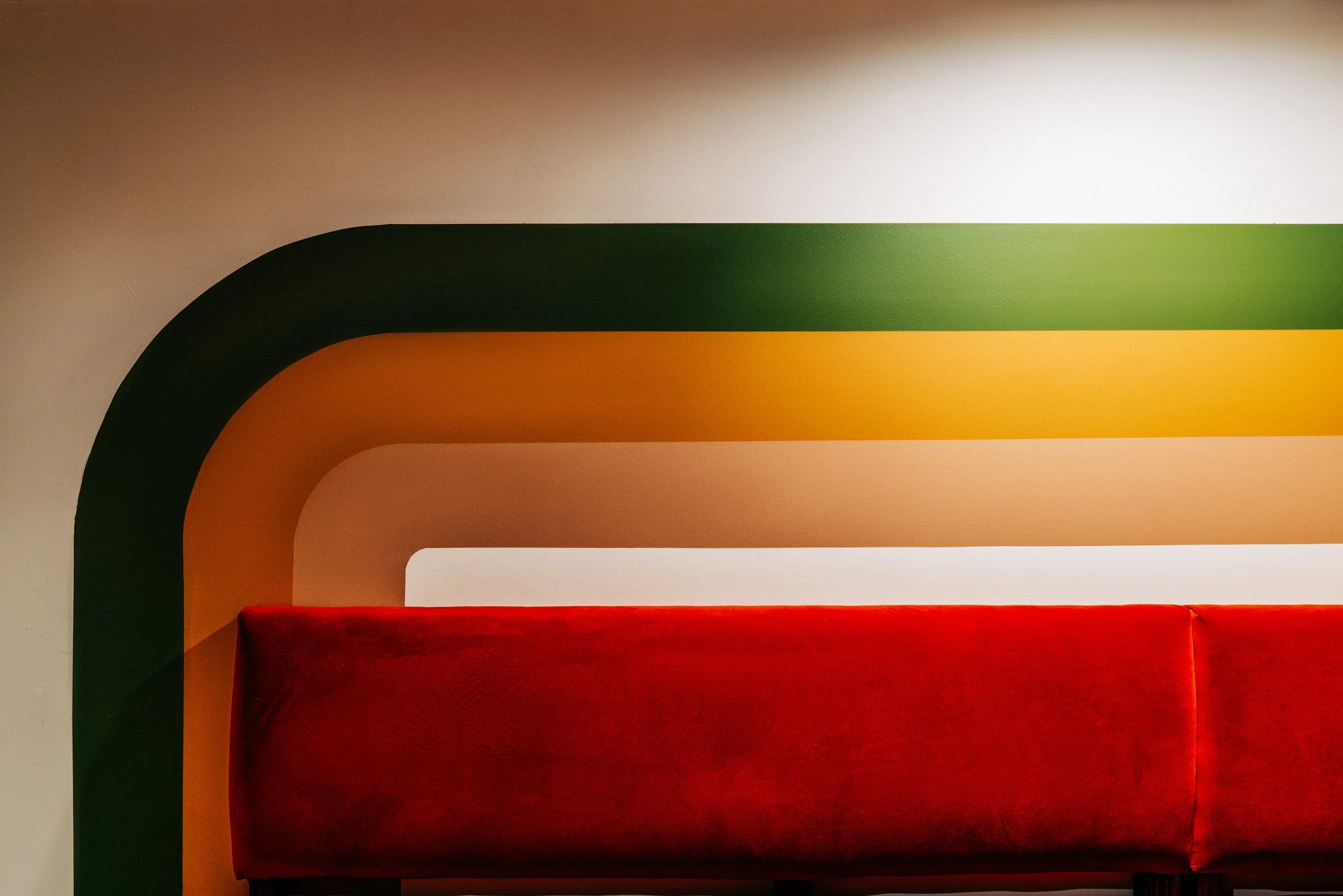 Chit Chat Lounge by Siren Betty Design, graphic wall pattern in green and gold framing vivid red banquette seating.