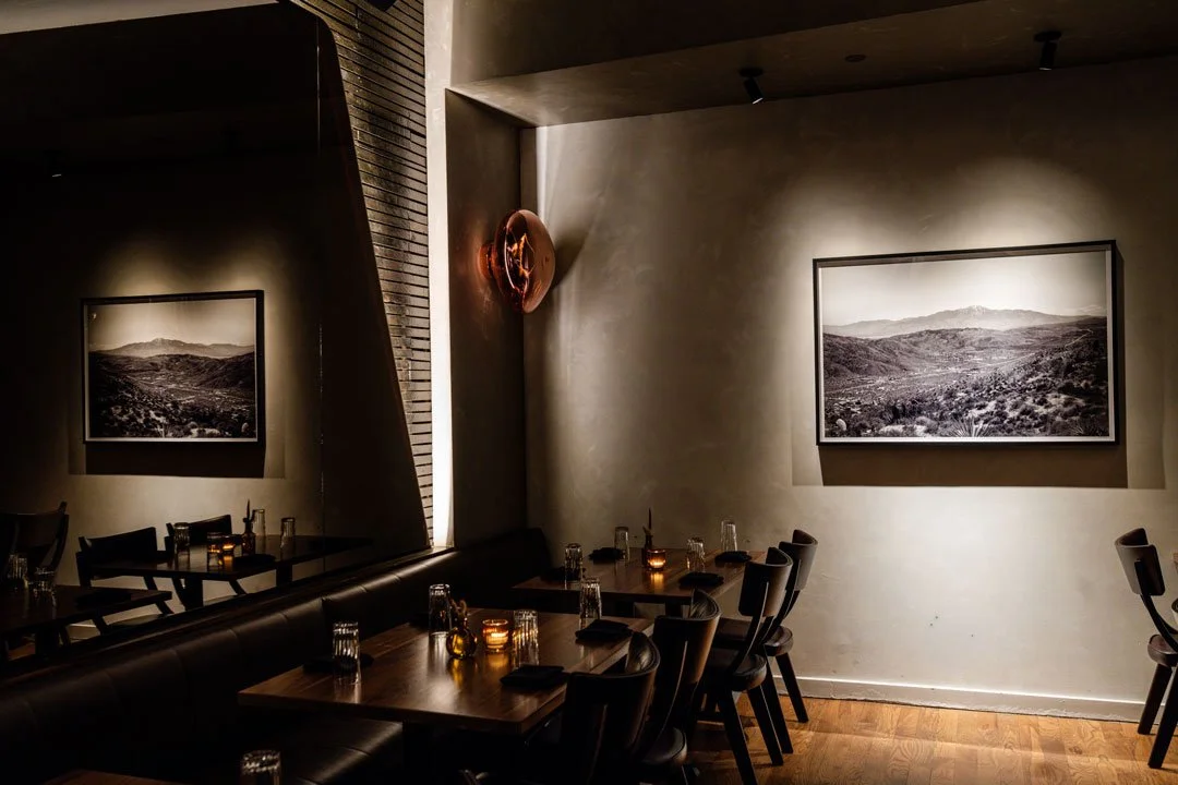El Che dining area by Siren Betty Design with a mirrored wall, leather banquettes, wood tables, and landscape photography.