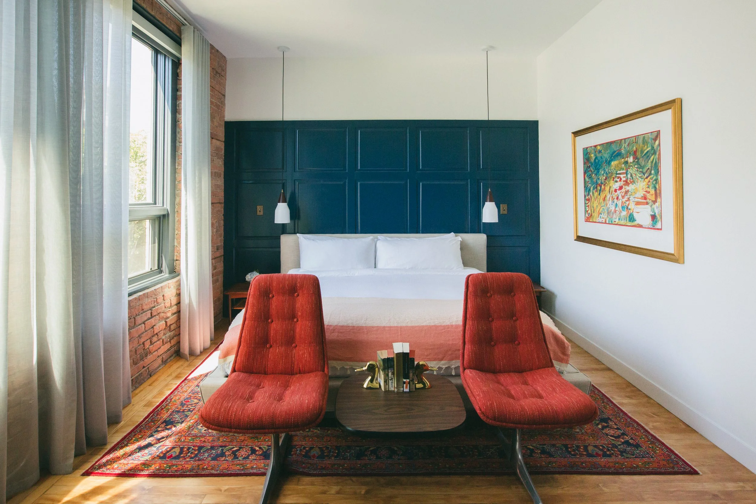 The Publishing House boutique guest room with navy wall paneling, exposed brick, vintage red chairs, and a Persian rug by Siren Betty Design.