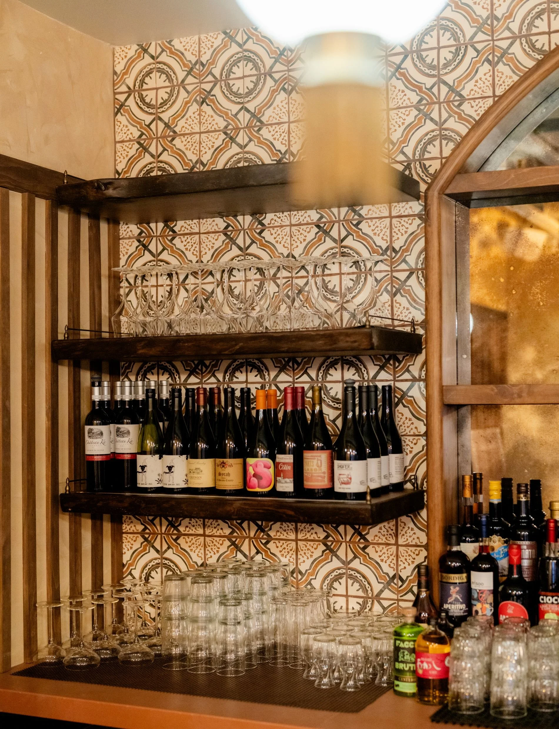 Custom tiled bar backsplash with wine bottles and shelving detail at Café Yaya by Siren Betty Design.