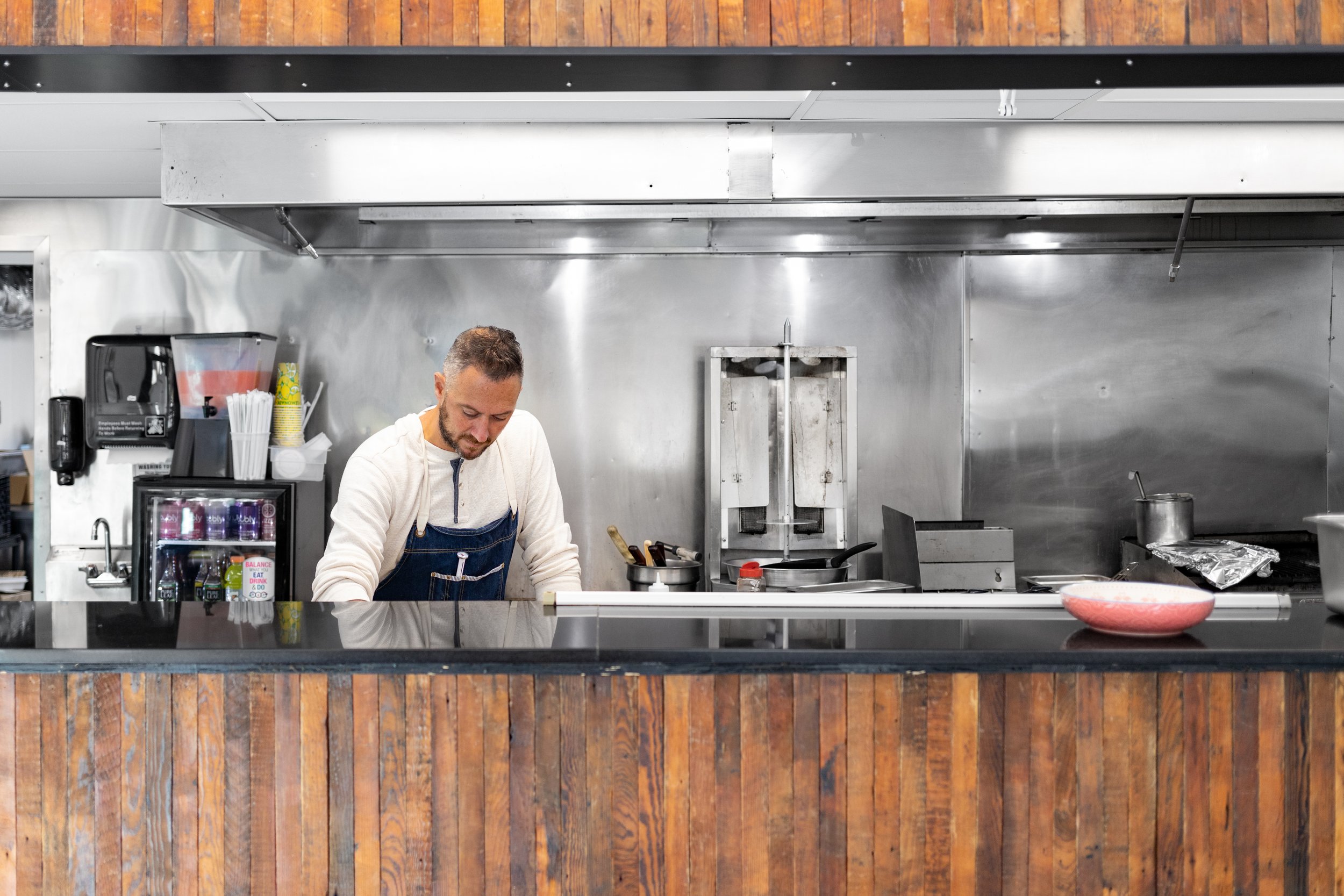 Chef prepares food behind rustic wood counter and stainless steel kitchen at Evette’s by Siren Betty Design.