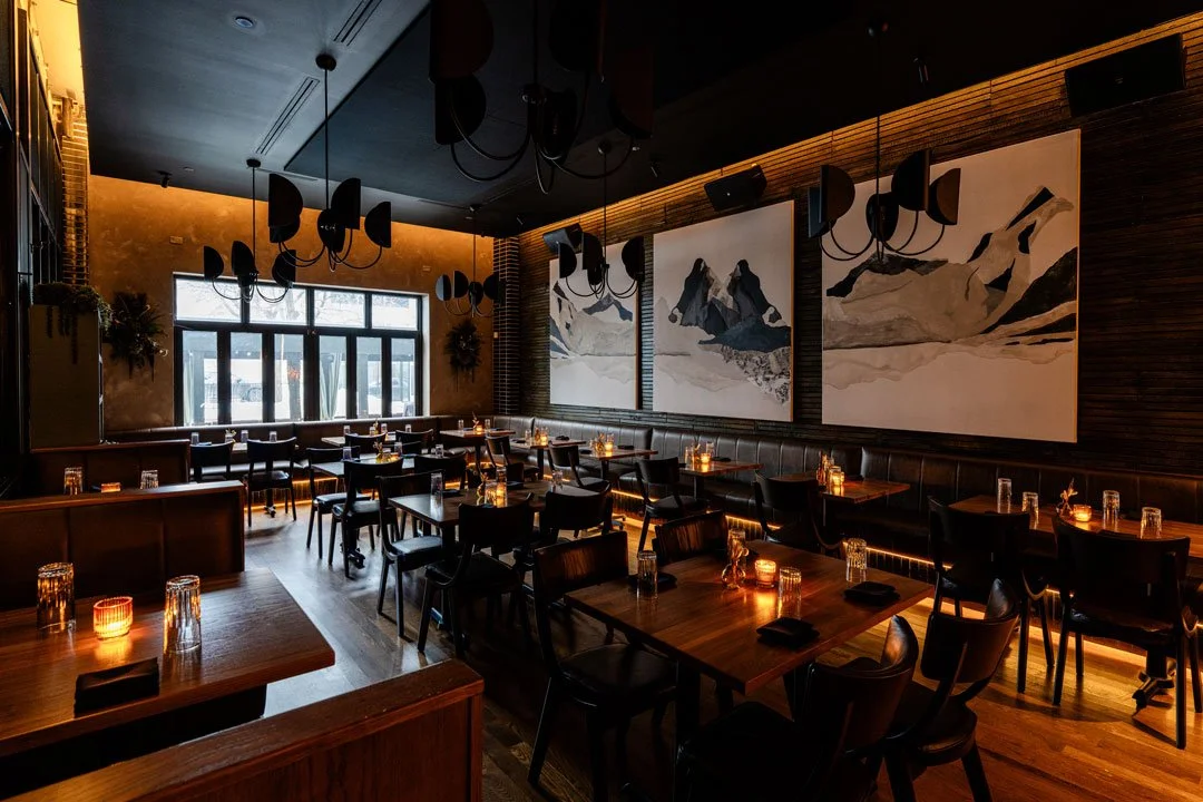 El Che dining room by Siren Betty Design with sculptural chandeliers, mountain artwork, leather banquettes, and warm amber lighting.