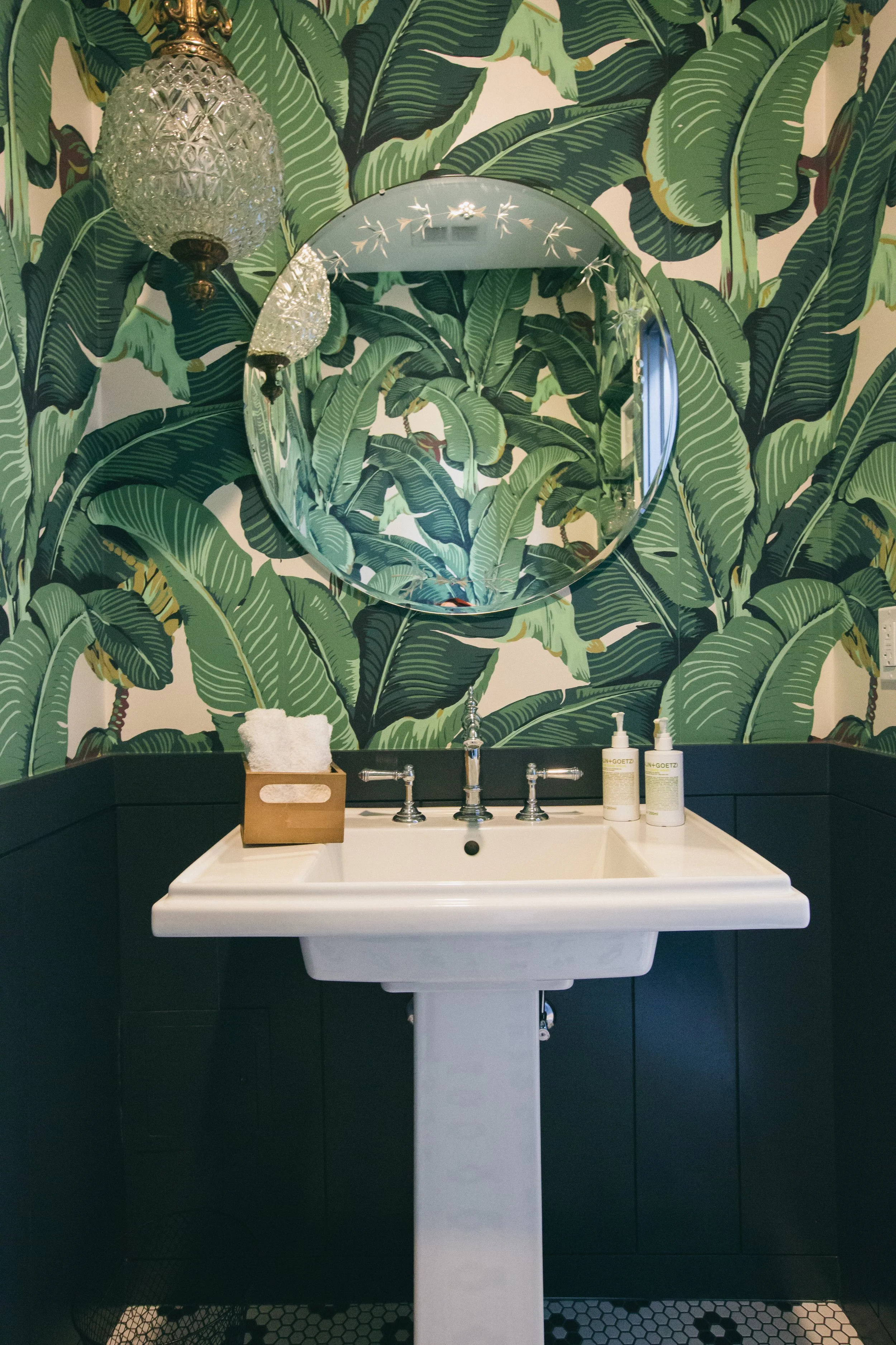 The Publishing House by Siren Betty Design, powder room with bold palm wallpaper, pedestal sink, and globe lighting.