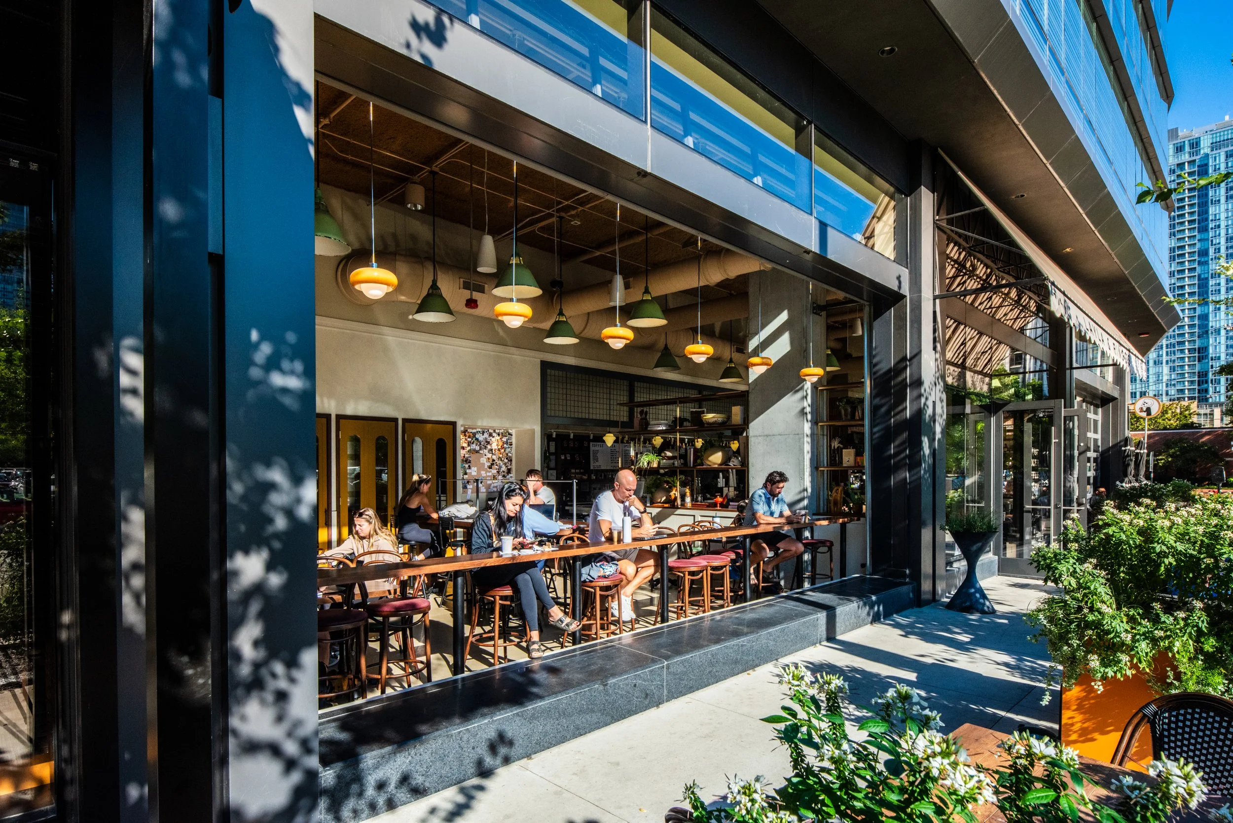 Layla and Ringo’s exterior with open windows, café seating, warm lighting, and street greenery designed by Siren Betty Design