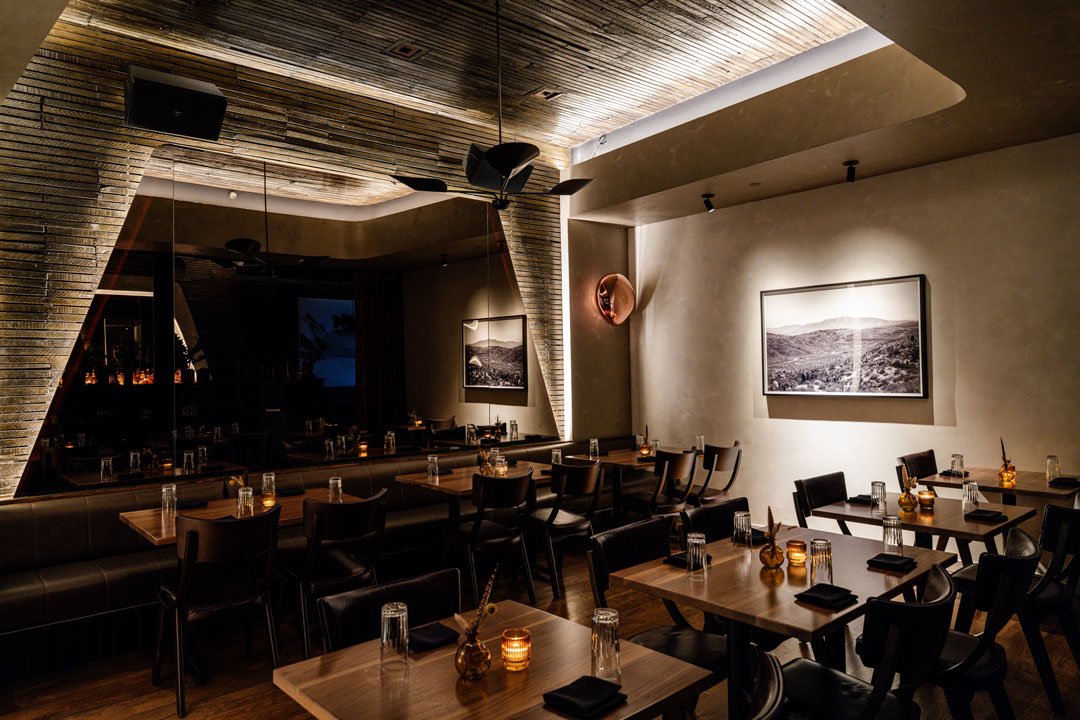 El Che restaurant interior by Siren Betty Design with illuminated brick ceiling, mirrored wall, landscape art, and candlelit wood tables.