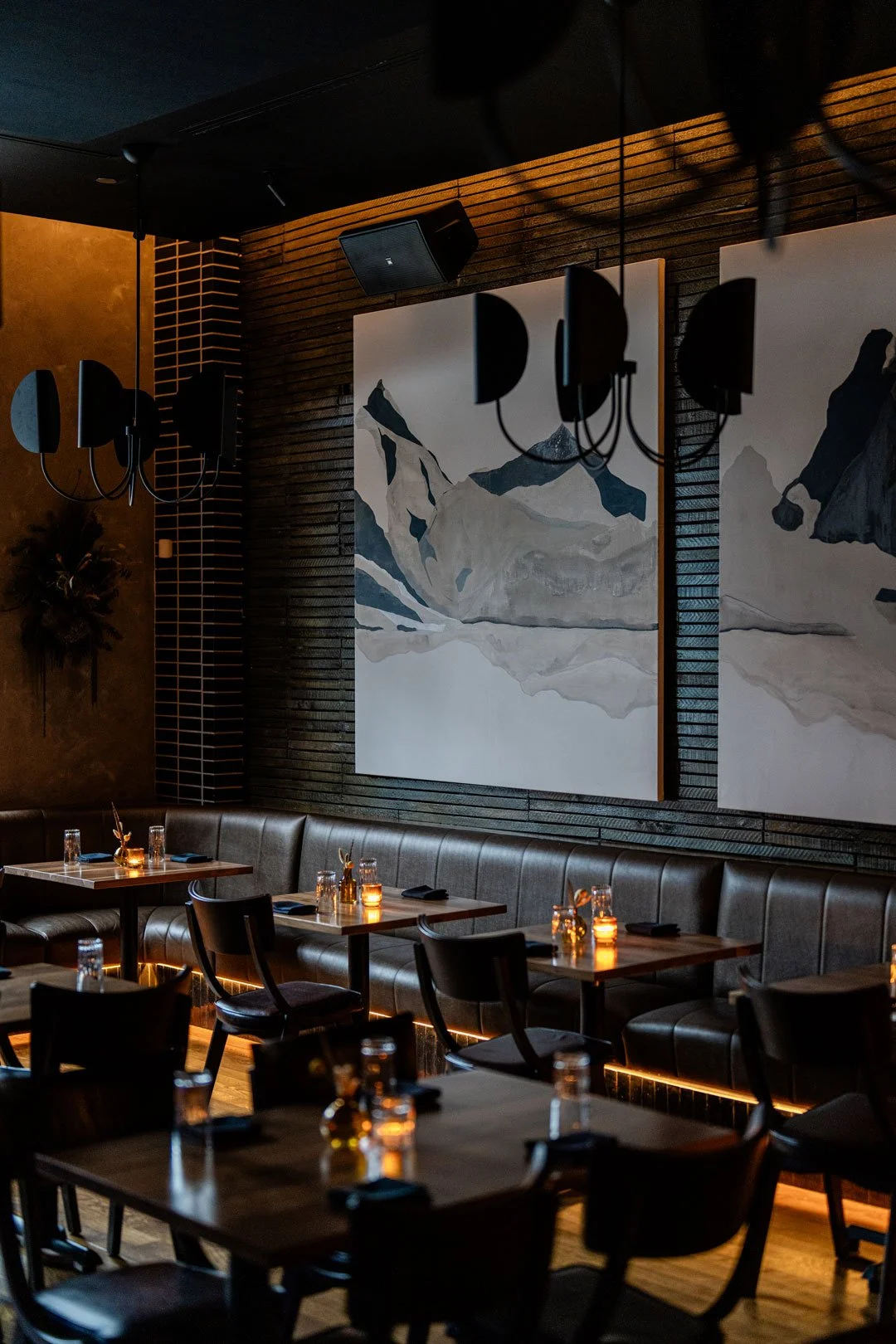 El Che dining room by Siren Betty Design with charcoal brick, sculptural chandeliers, leather banquettes, and oversized mountain artwork.