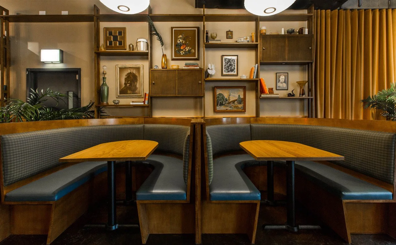 Monty’s Tap by Siren Betty Design, curved wood booths with plaid upholstery framed by wall art and warm lighting.
