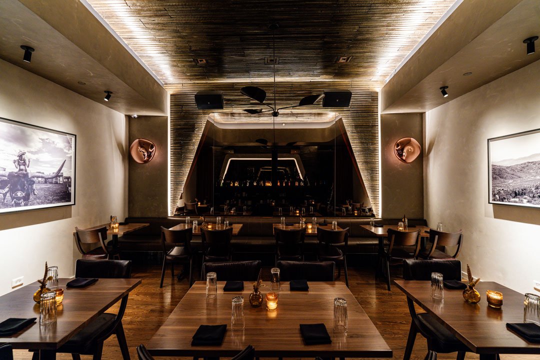 El Che restaurant interior by Siren Betty Design with black leather banquettes, warm wood tables, sculptural lighting, and mirrored walls.