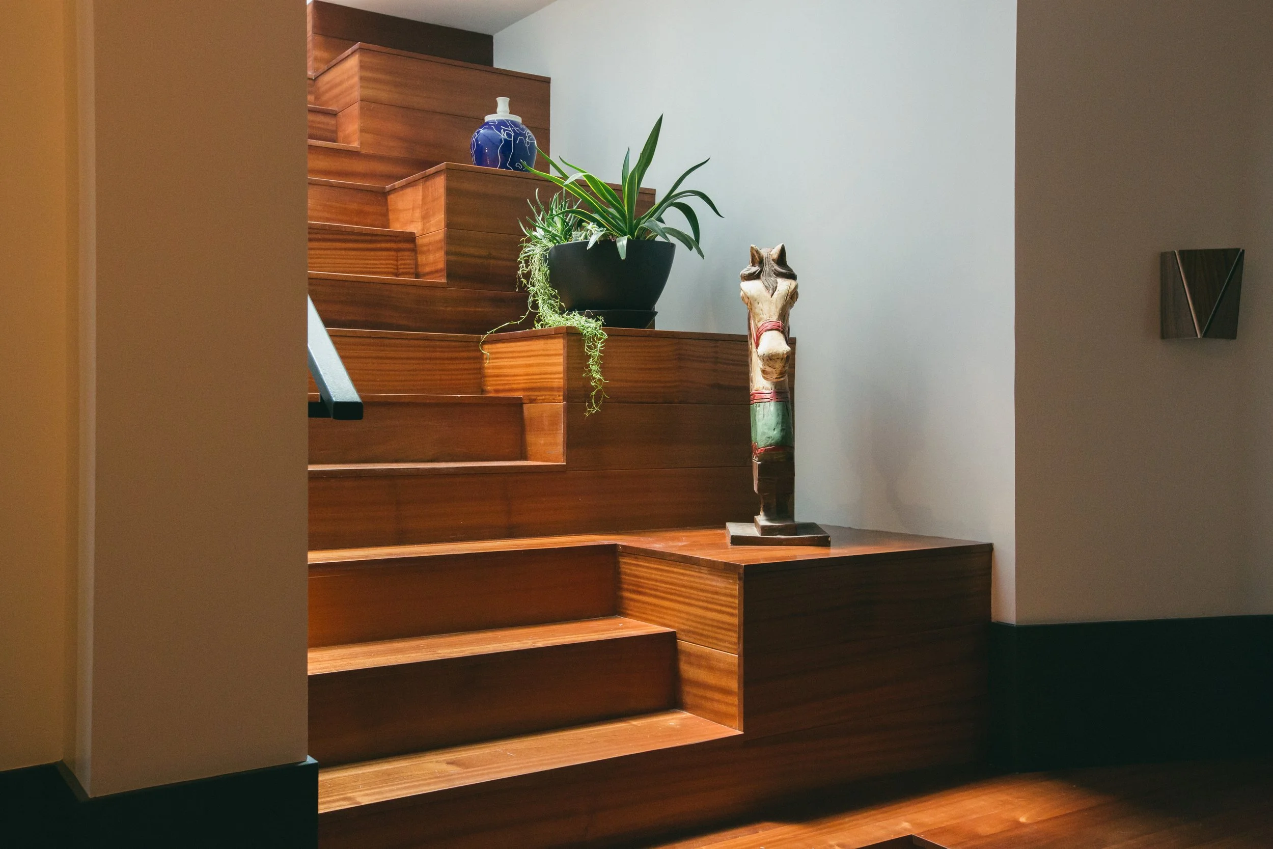 Restored wood staircase at The Publishing House styled with tiered plants, ceramics, and a carved horse sculpture by Siren Betty Design.