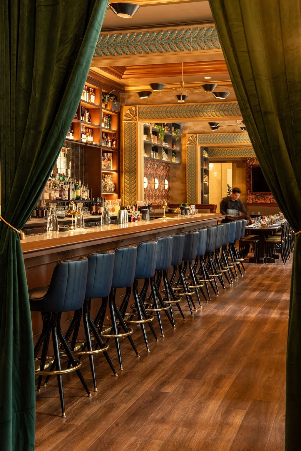 Eaves restaurant bar framed by green velvet curtains, blue stools and ornate millwork by Siren Betty Design.