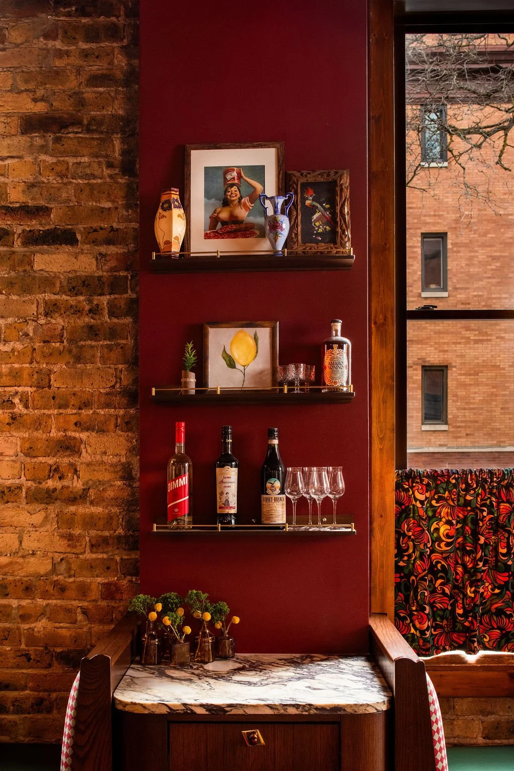 Styled shelving with wine and artwork against red wall at Dimmi Dimmi by Siren Betty Design.