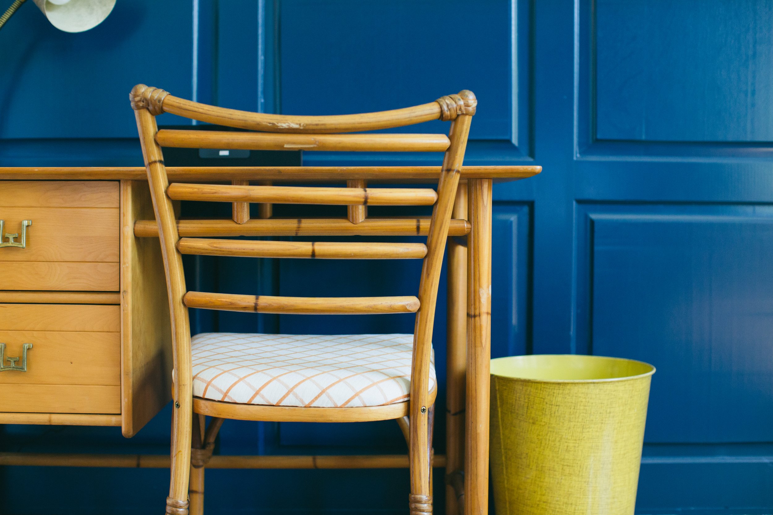 The Publishing House by Siren Betty Design, rattan chair and wood desk against navy paneled wall with yellow accents