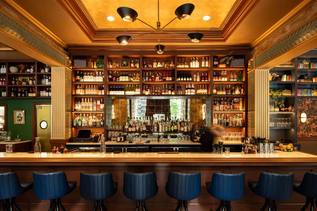 Custom wood bar at Eaves with blue stools, mirrored shelving and a luminous gold ceiling by Siren Betty Design.