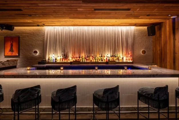 Hide & Seek cocktail bar by Siren Betty Design, moody lighting with marble bar, soft drapery backdrop, and modern barstool seating.