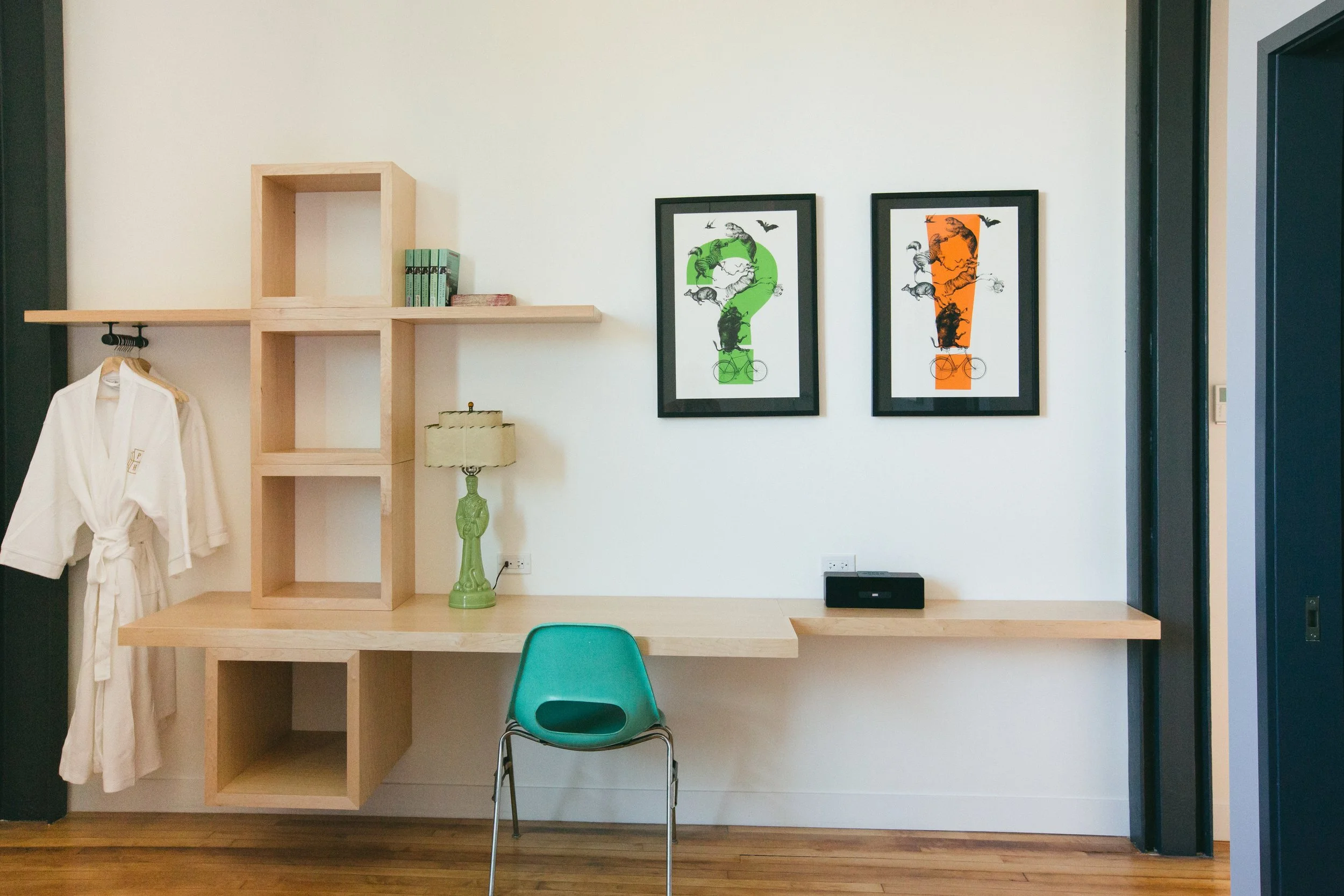 Custom maple desk and open shelving in a Publishing House guest room with a teal midcentury chair and curated artwork by Siren Betty Design.
