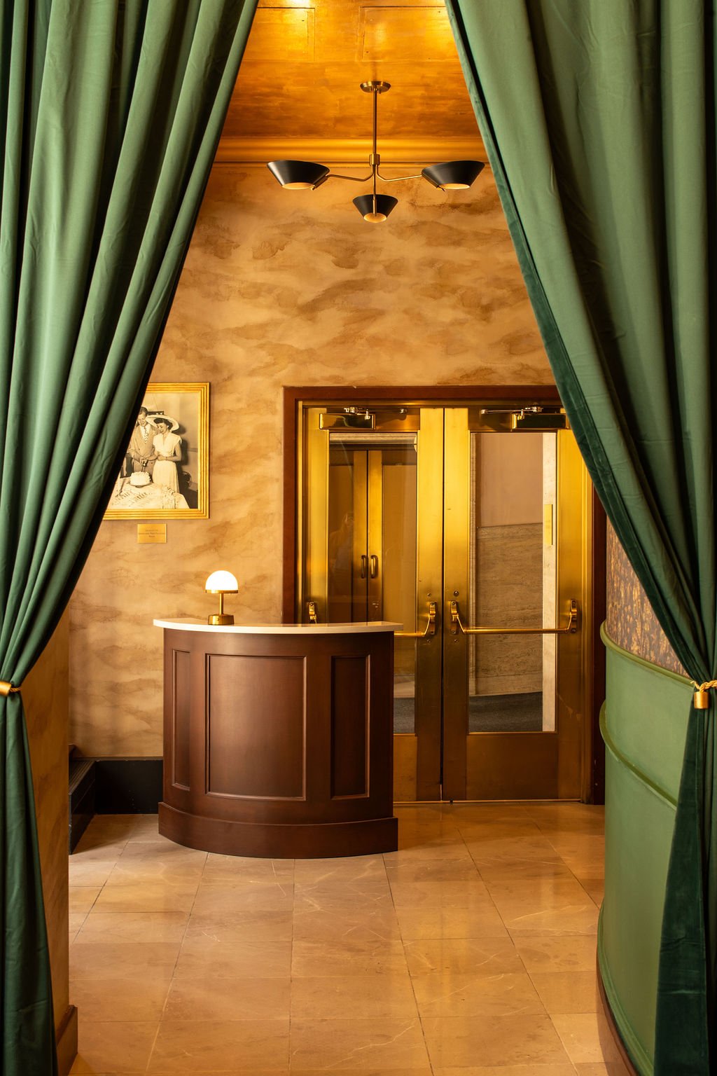 Eaves host stand and brass doors framed by green velvet drapery by Siren Betty Design.