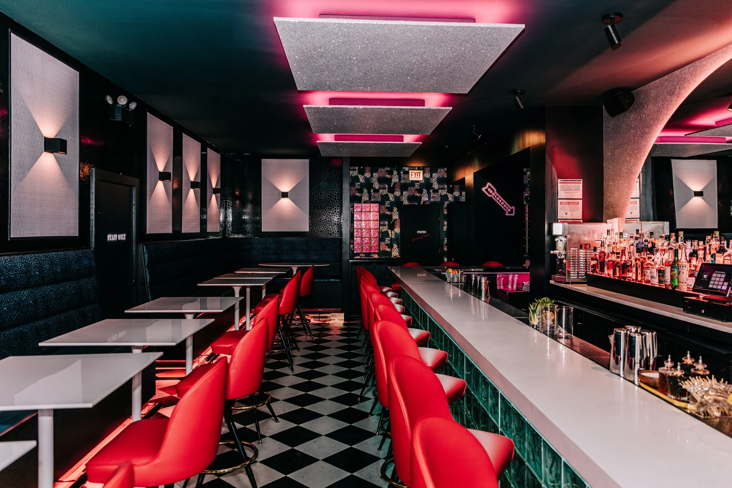 Common Decency by Siren Betty Design featuring vibrant red bar chairs, glass-block lighting, and checkered floors for a dynamic modern bar scene.