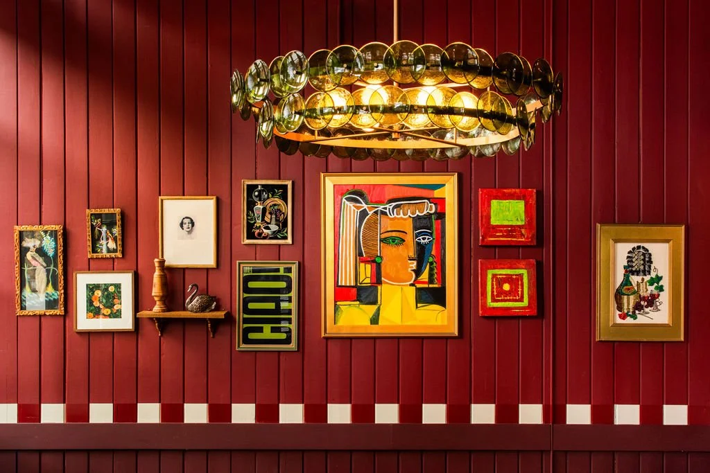 Colorful gallery wall and chandelier against red paneling at Dimmi Dimmi by Siren Betty Design