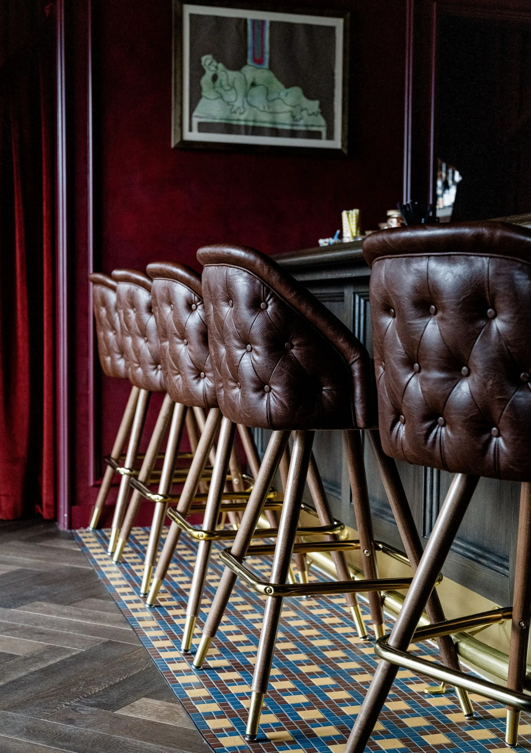 Row of tufted leather bar stools lined against the dark wood counter at The Anteroom Chicago, by Siren Betty Design.