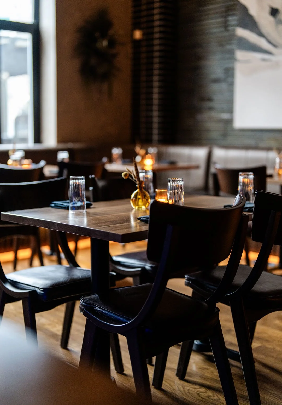 El Che table detail by Siren Betty Design with dark wood furniture, black leather chairs, candlelight, and softly lit banquette seating.