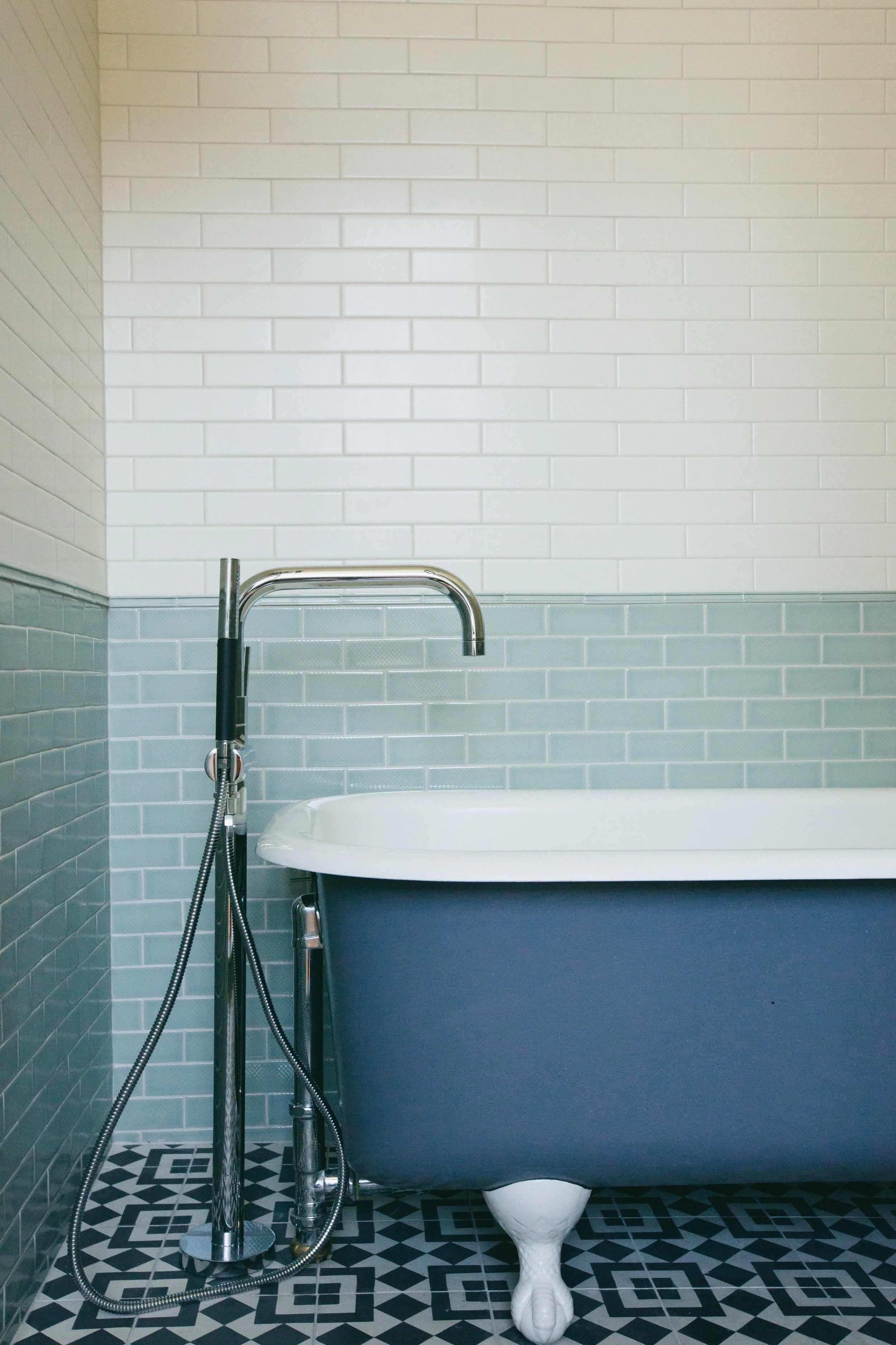 The Publishing House by Siren Betty Design, white clawfoot tub with blue tile wainscoting and patterned mosaic floor.