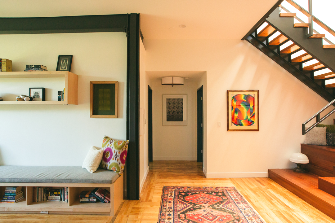 The Publishing House guest suite lounge with built-in window seating, custom shelving, vintage artwork, and a warm wood staircase by Siren Betty Design.