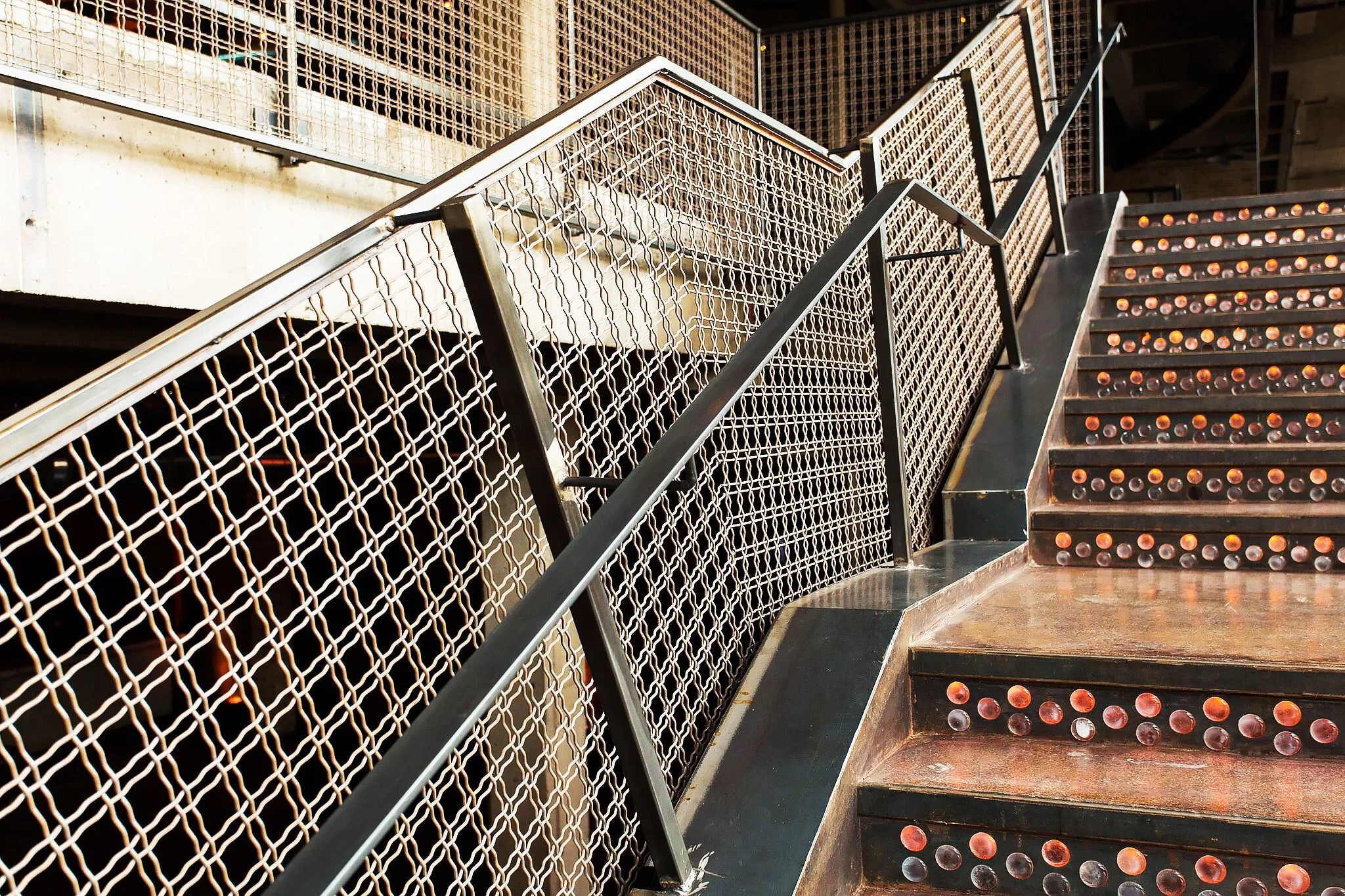 Morgan MFG by Siren Betty Design. Stair detail with perforated metal railing and risers set with round amber lenses.
