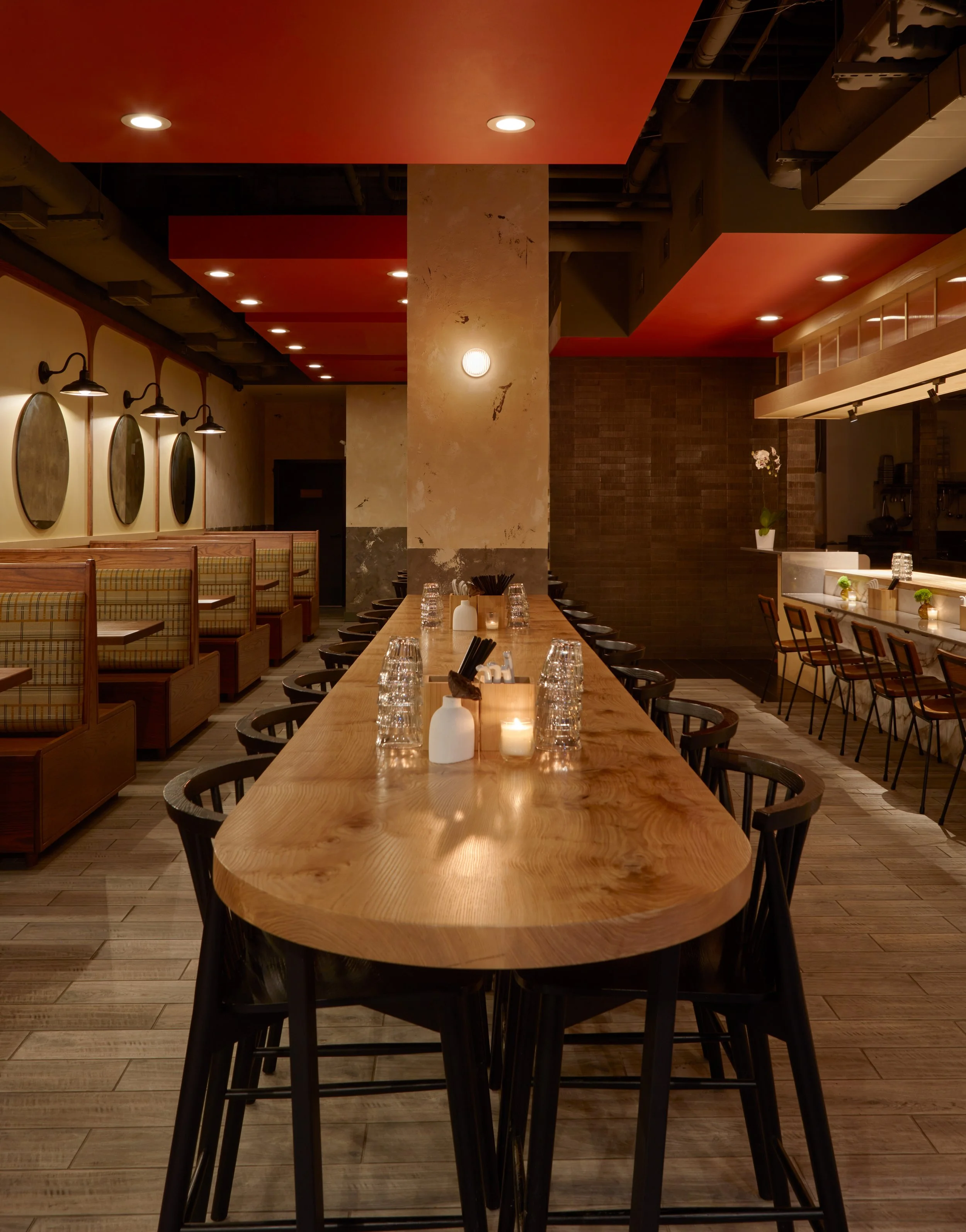 Long wood dining table at Akahoshi Ramen by Siren Betty Design with soft lighting, warm red ceiling, and modern booth seating.