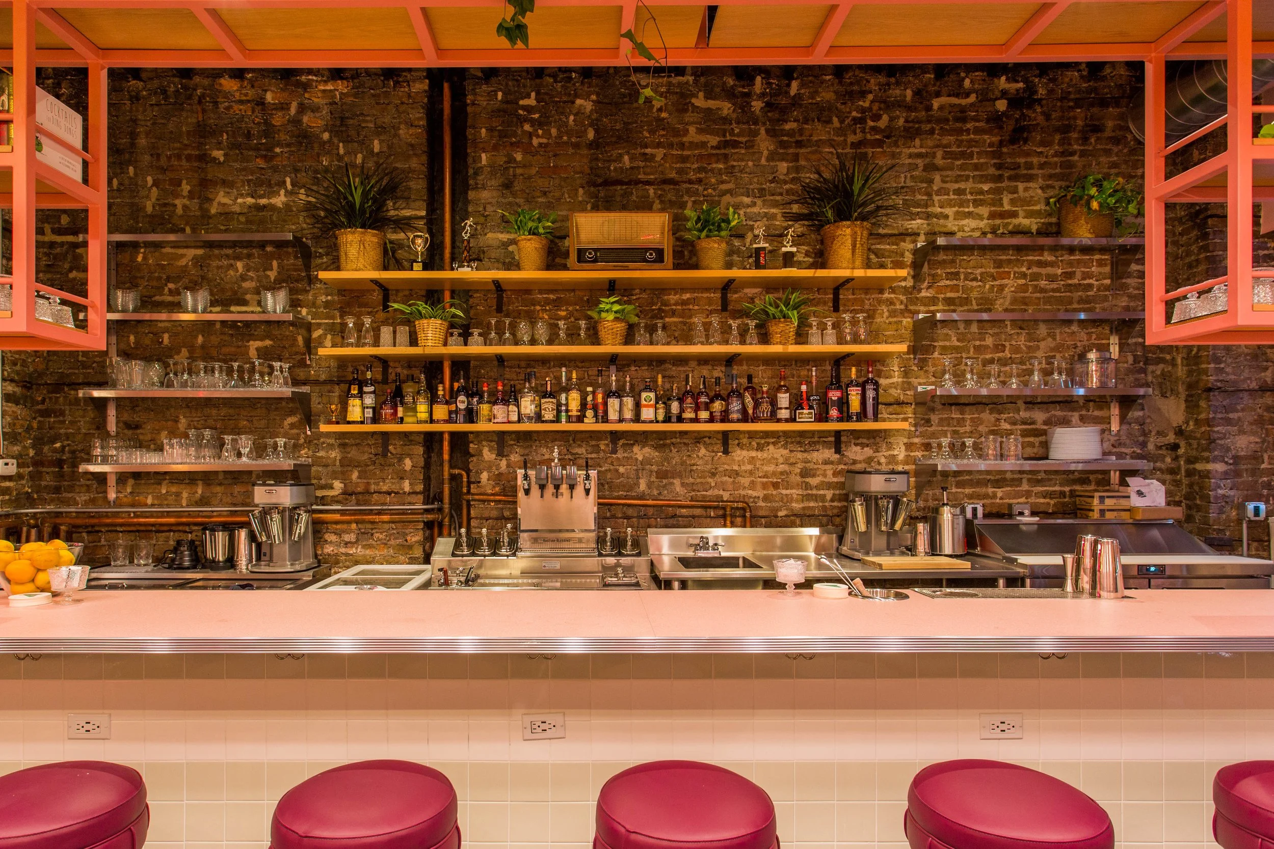 Pink Squirrel by Siren Betty Design, Chicago cocktail bar with pink countertop, brick wall, and open shelving.
