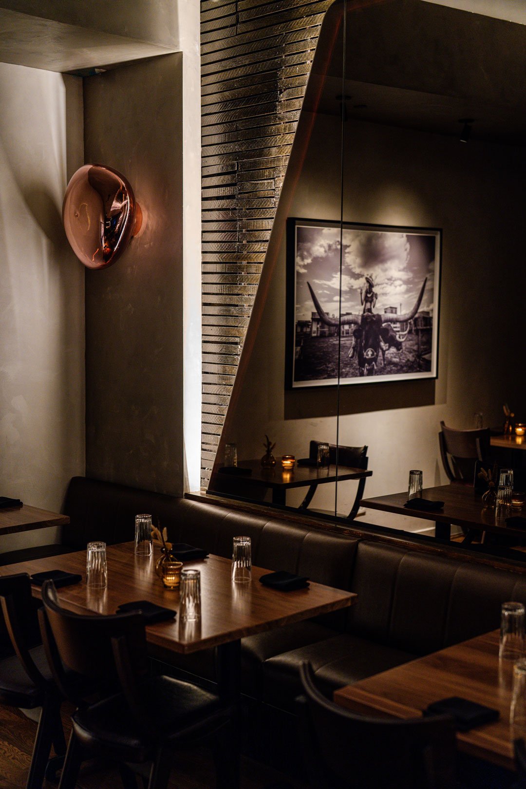 El Che interior detail by Siren Betty Design with a copper wall sconce, mirrored wall, framed ranch photography, and leather seating.